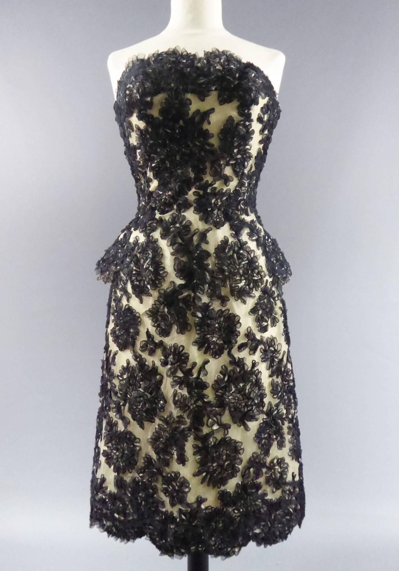 Ca. 1960

Frankreich

Haute Couture Carven Kleid. Ein Bustier mit Basken im Rücken mit vier Bändern aus schwarzem Samt. Stickerei aus schwarzen Organzabändern auf cremefarbenem Tüll. Petticoat aus Tüll und Faltenrock unter dem Kleid. Reißverschluss