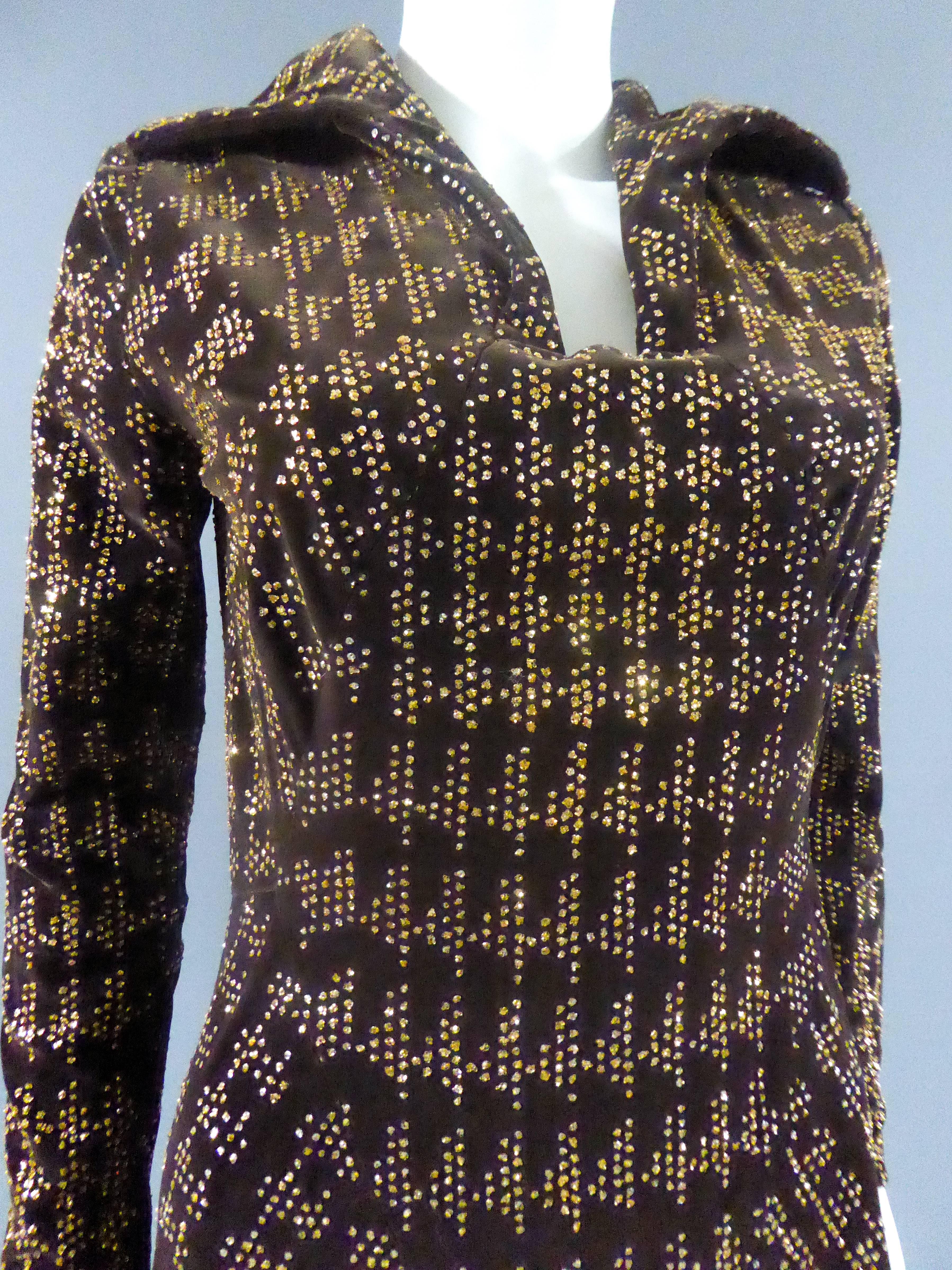 Um 1975

Frankreich

Langes Kleid mit weitem Rock aus braunem Samt mit goldenem Glitter, der in geometrischen Mustern und Hahnentrittmuster aufgeklebt ist. Offener Hemdkragen auf schmaler und rechteckiger Brust. Reißverschluss im Rücken und Kragen