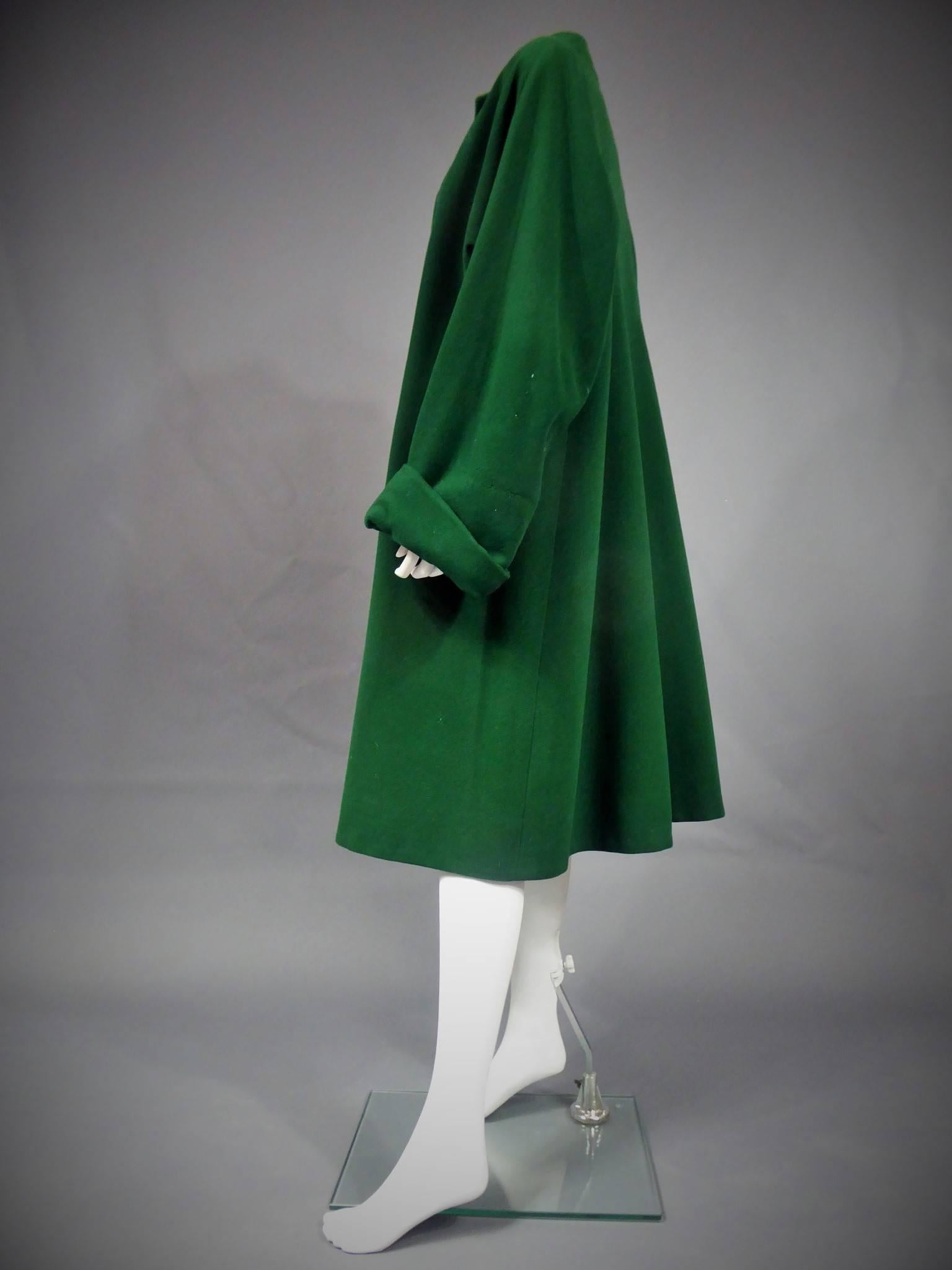 Circa 1955/1965
Paris, France 
Large coat in thick felt green wool by Bruyère. Large sleeves 3/4 raglan wide lapel, large trapeze shape. Two pockets on the sides. Black lining in silk taffeta. Back, detail of panels returning to the shoulders. Black