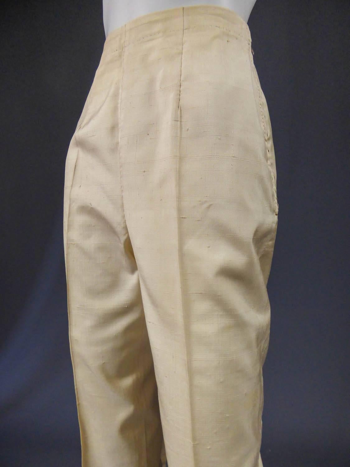 Circa 1960

Italy

High-waisted straight cut pants in ivory wild silk shantung. Without belt, with a work of pleats from the waist. Side metal zipper on the hips. Small button tab at the closure. Darts widened origins and hand finish. Label white