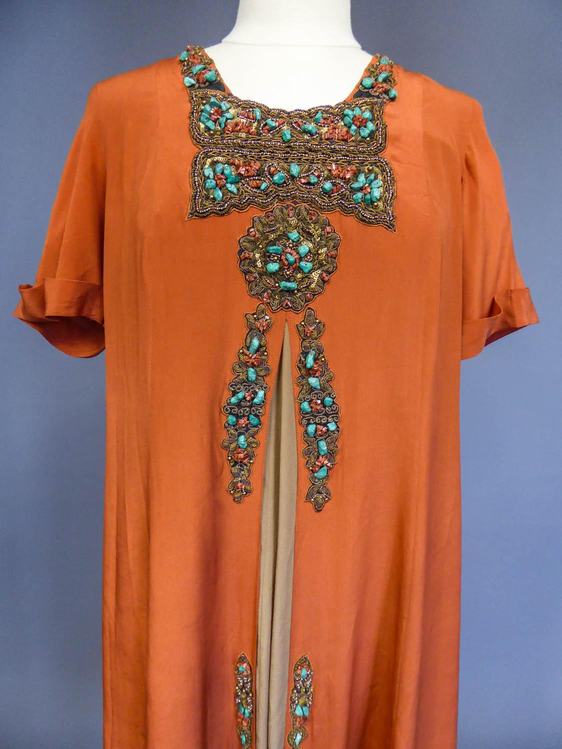 Circa 1960
Europe

A surprising little jewel dress in the orientalist style of the 1920s. Orange rust silk crepe with rich embroidery of pearls, sequins and gold chenilles, all set with oranges raw stones and turquoises! Small short sleeves with
