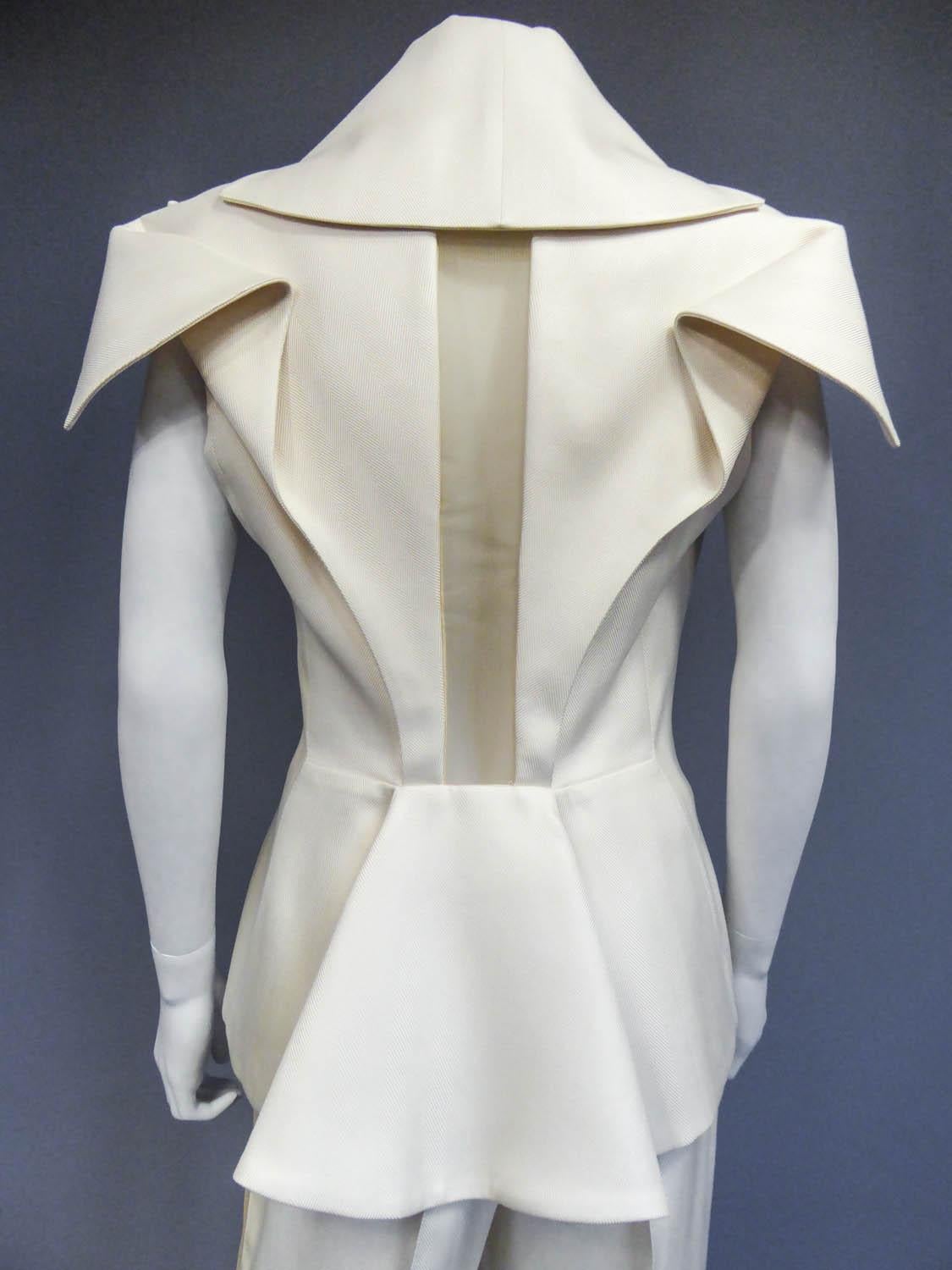 Circa 2000

England

Alexander Mcqueen jacket and trousers suit in cream silk twill. The originality of this set is characterized by the back cut of the jacket, openwork in the center, and marked by large lapels on the shoulders and a folded back