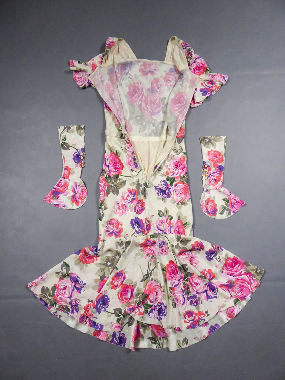 Circa 1985
France

Jeanne Lanvin summer dress in cream satin prints with patterns of roses in shades of pink, purple, coral and khaki. Straight collar, ruffle sleeve and removable cuffs covering the hand and simulating fingerless glove, closing with