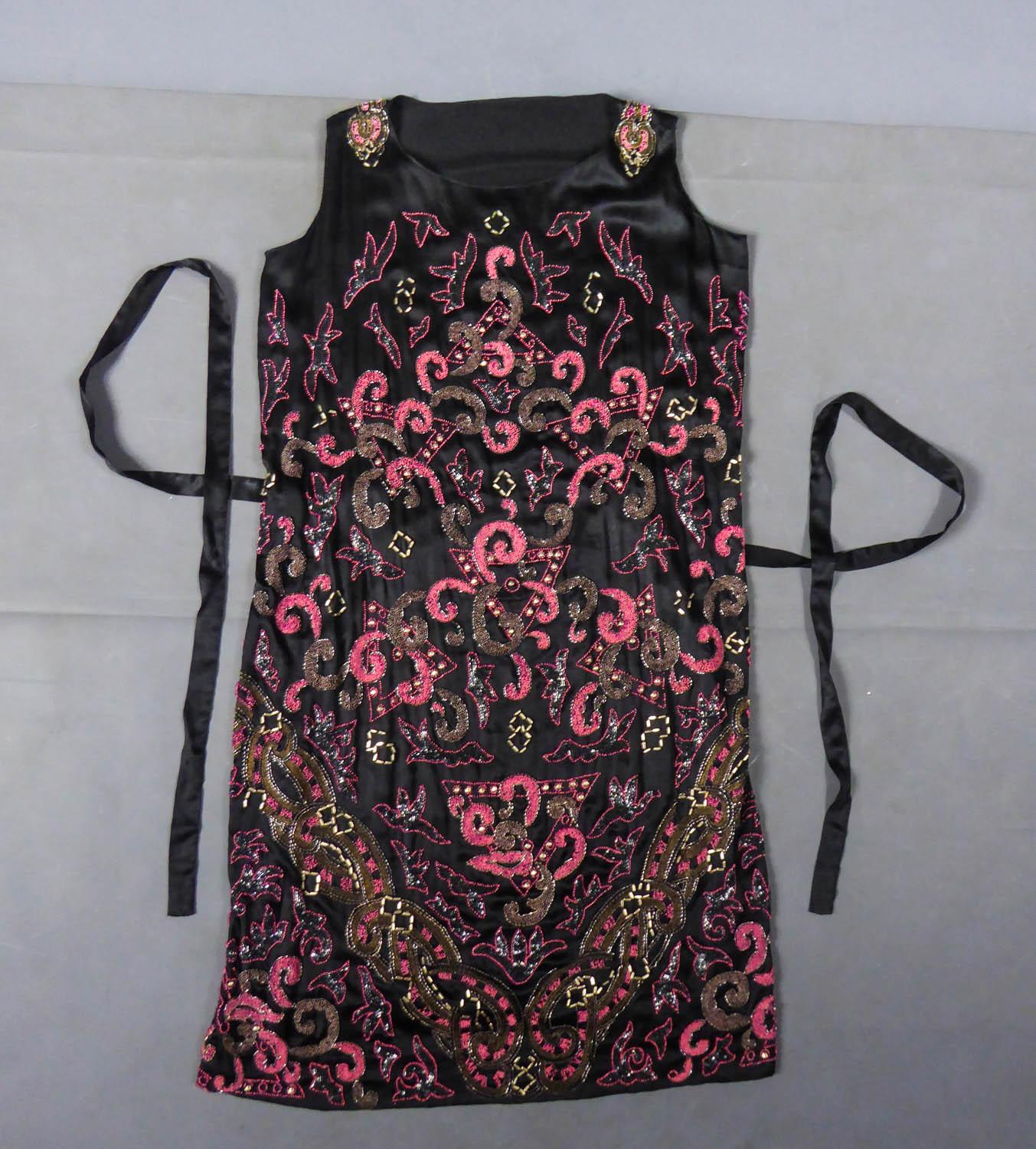 Circa 1925
France

Charleston evening dress from the Art Deco period in black duchess satin embroidered with silver cabochons, pink and black glass beads and iridescent tubular beads. Straight sleeveless dress with baroque decor in the Bizarre taste