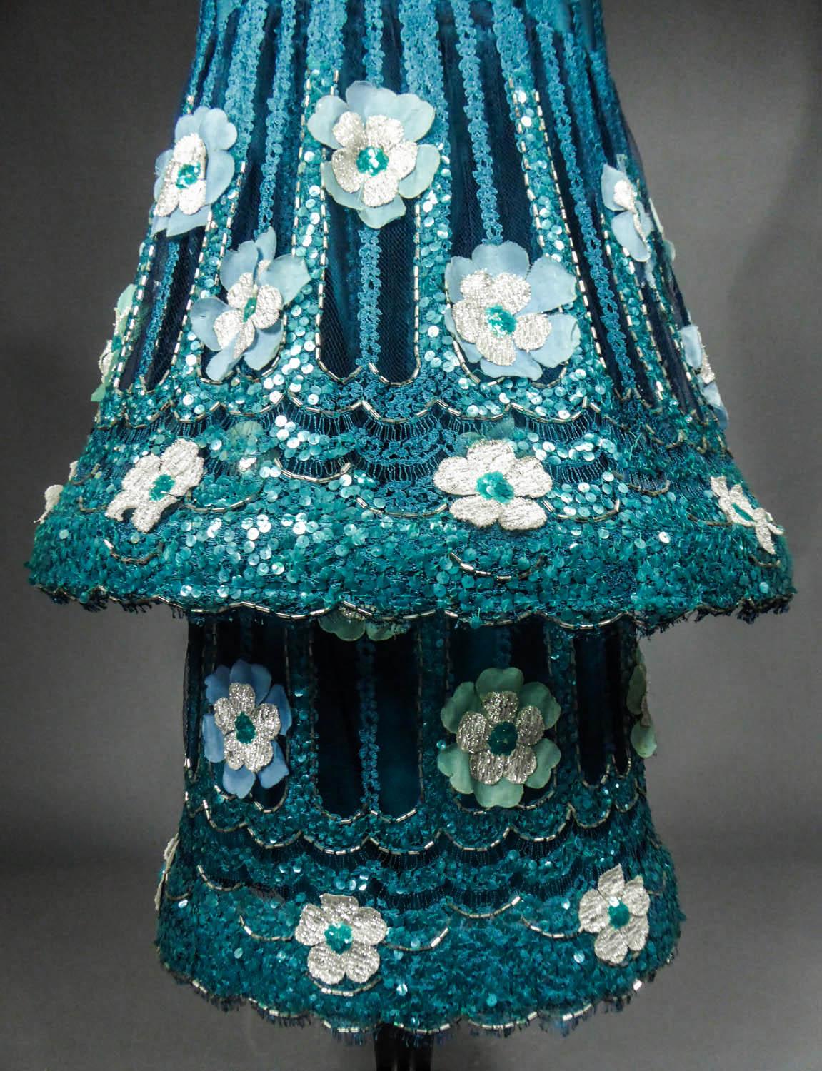 Circa 1968/1970
Paris France

A tubular tulle dress with hoop and turquoise blue lace embroidered with iridescent blue sequins and translucent tubular sequins. Large blue-sky and silver lurex daisies appliqué. Three-quarter straight sleeves and