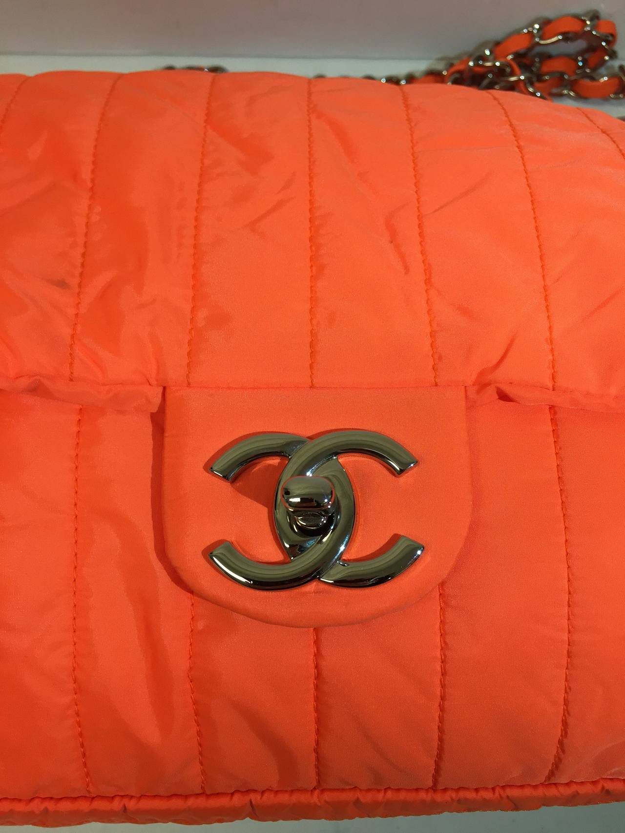 This is an authentic CHANEL Nylon Vertical Quilted Jumbo Flap in neon orange. This relaxed flap bag is made of a casual nylon material with a unique vertical quilting, and is crafted in the classic flap bag structure. The handles are made of leather