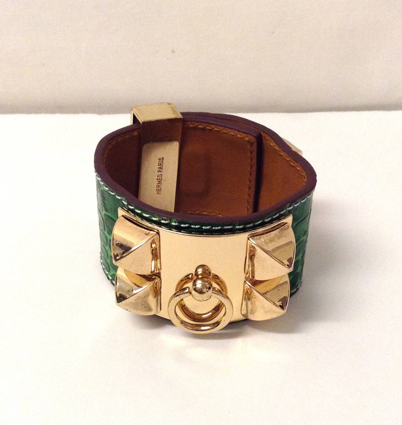 This is an authentic HERMES Shiny Alligator Collier De Chien CDC Bracelet in Small Emerald Green This stylish bracelet is crafted of Green alligator skin and features two palladium silver plates, one with decorative studs and a dangling ring, and