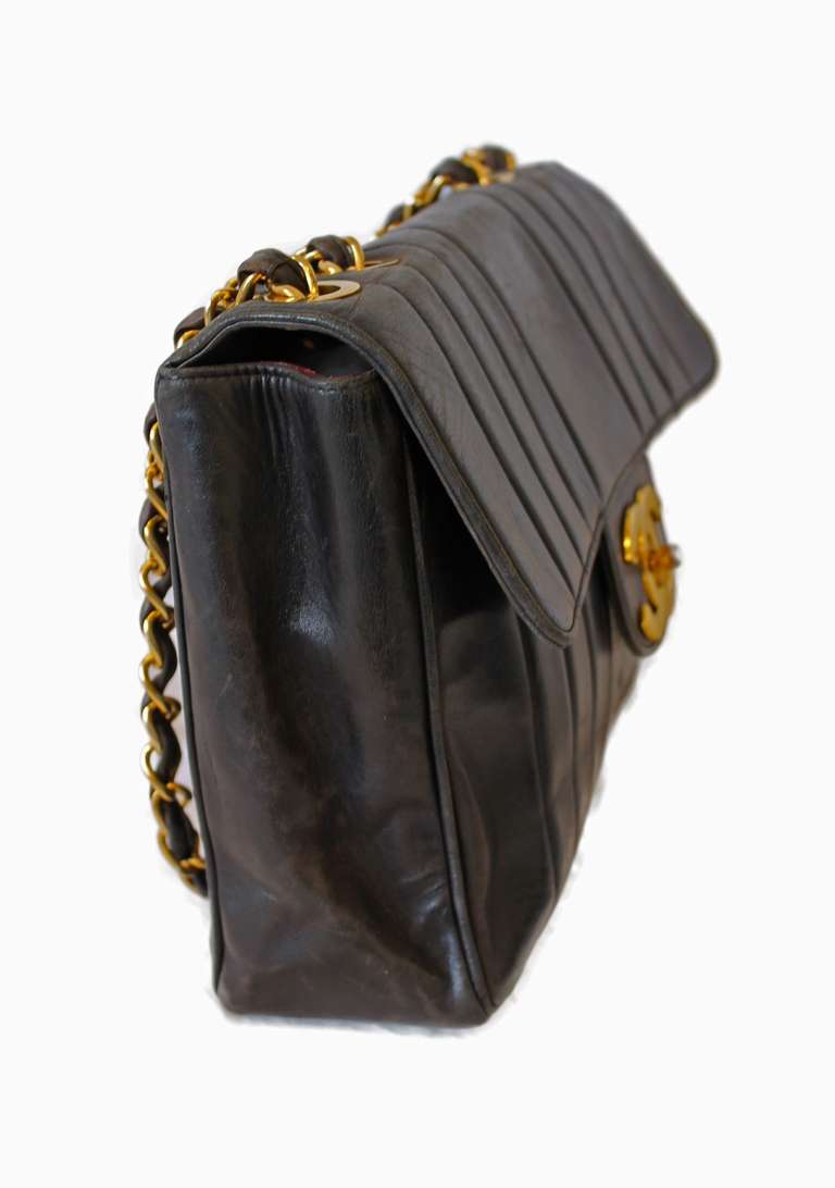 Specifics: Chanel vintage large classic flap bag in black lambskin. Features gold chain link double straps woven with black leather, vertical stitching along the front and back and a gold CC turn lock. Leather interior with zipper and patch pockets.