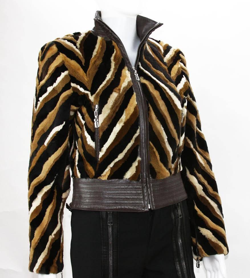 Intricately detailed jacket constructed with different shades of mink (black, browns and off white) forming a large chevron pattern. The leather trim at the neck and hem are stitched in multiple rows giving a ribbed effect. Encased in leather is a