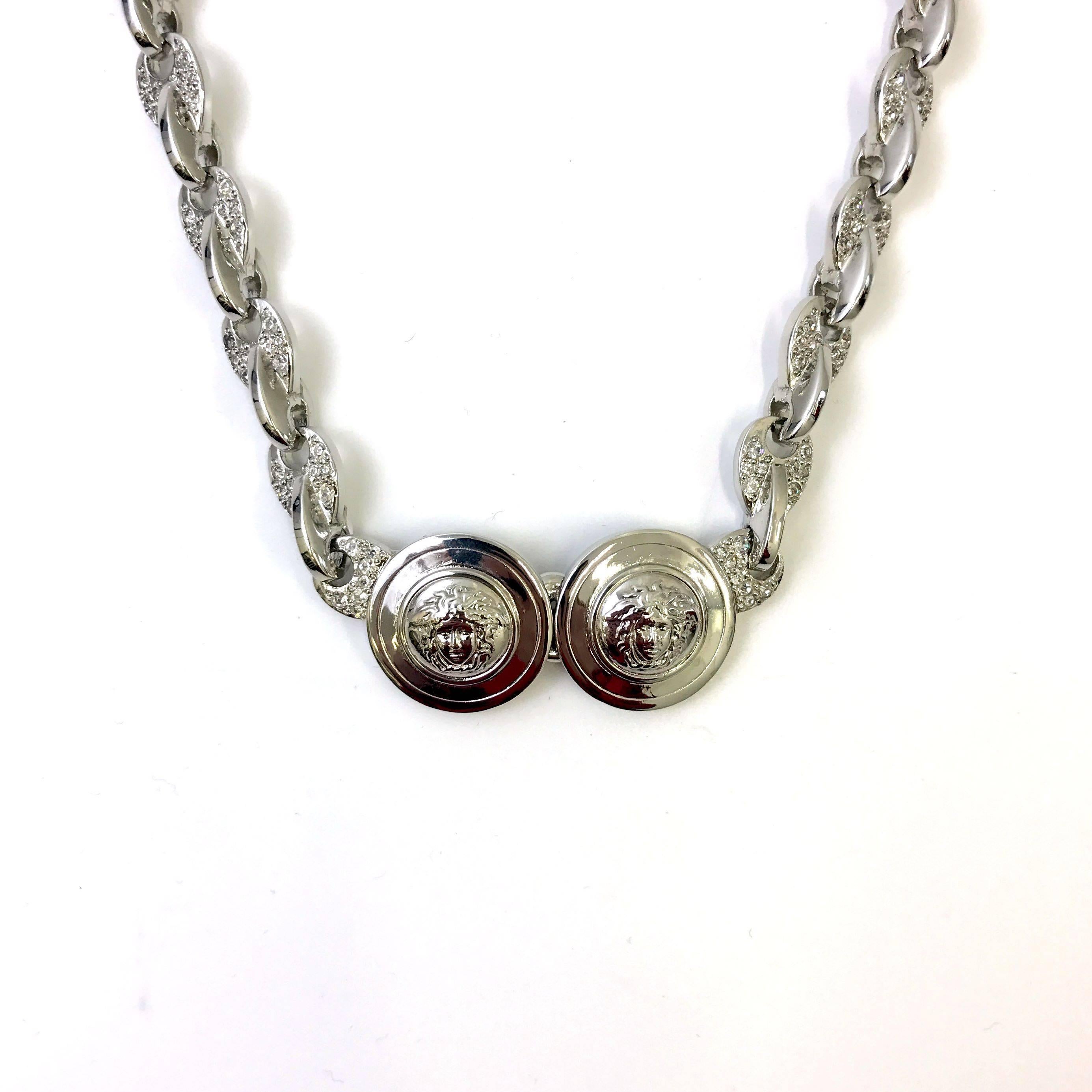 This is a iconic necklace from the famous Italian designer Gianni Versace from the 1990s. The necklace features a silver toned metal chain with a unique style link covered in rhinestones. In the centre of the chain there are two circle medallions