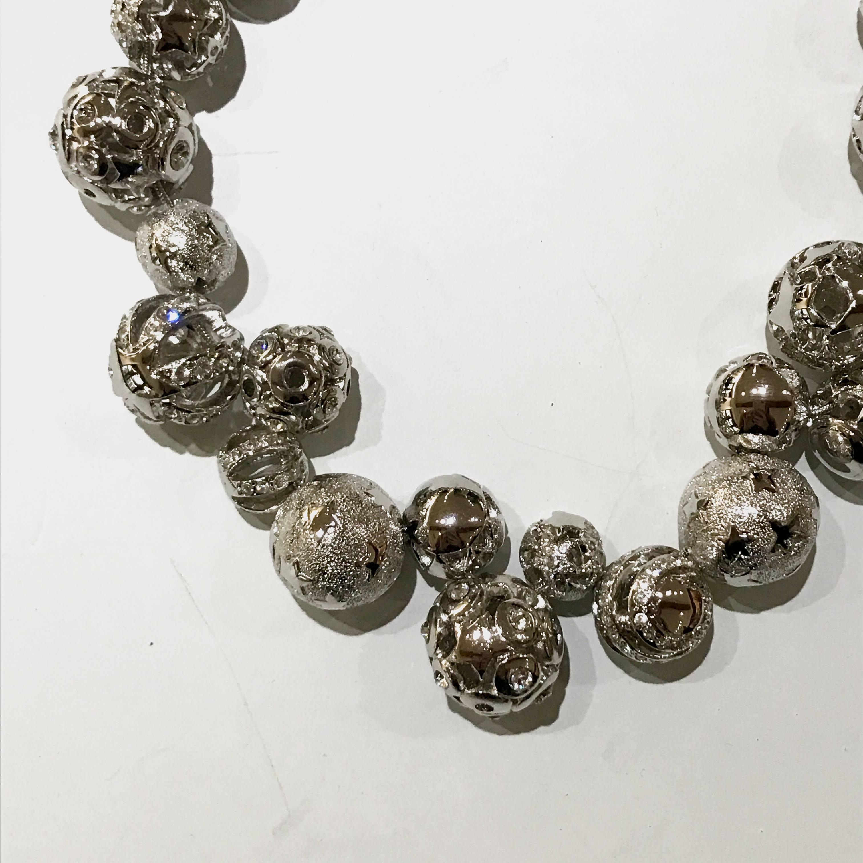 Este collar de Gianni Versace es único por sus detalles de bolas con diferentes motivos recortados. El tono plateado se complementa a la perfección con las piedras brillantes. Las bolas están hechas a mano individualmente y son únicas en sí mismas,