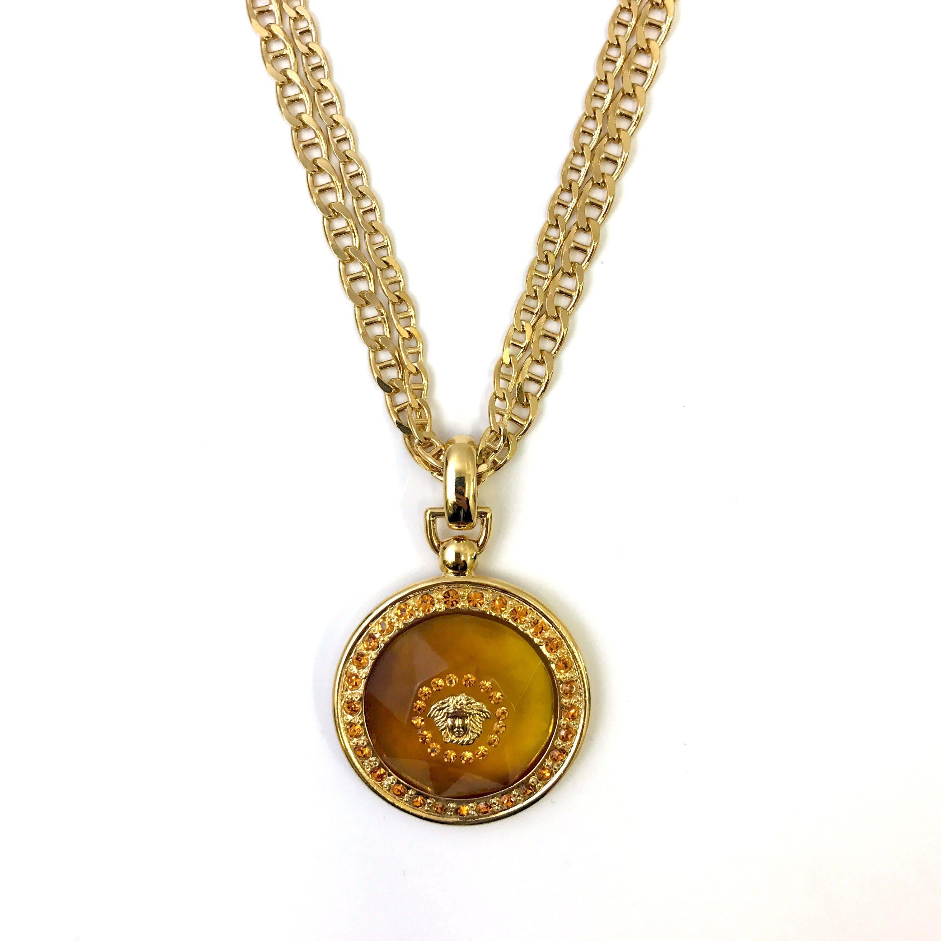 This traditional Gianni Versace pendant necklace is a staple piece for any Versace enthusiast. The lightweight gold tone chain features a double anchor styled chain with a orange clear plexiglass circular pendant dropping. The outer perimeter is