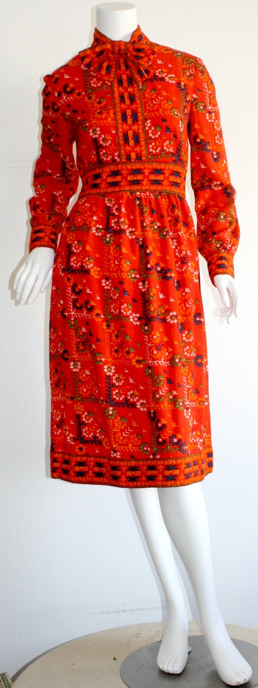 Wunderschönes Vintage 1960er Mollie Parnis Kleid!!! Leuchtend roter Hintergrund mit farbenfrohem Tribal-Print. Angenähte Kätzchenschleife im Nacken. Verdeckter Reißverschluss auf der Rückseite. Kann problemlos vom Tag in die Nacht übergehen.