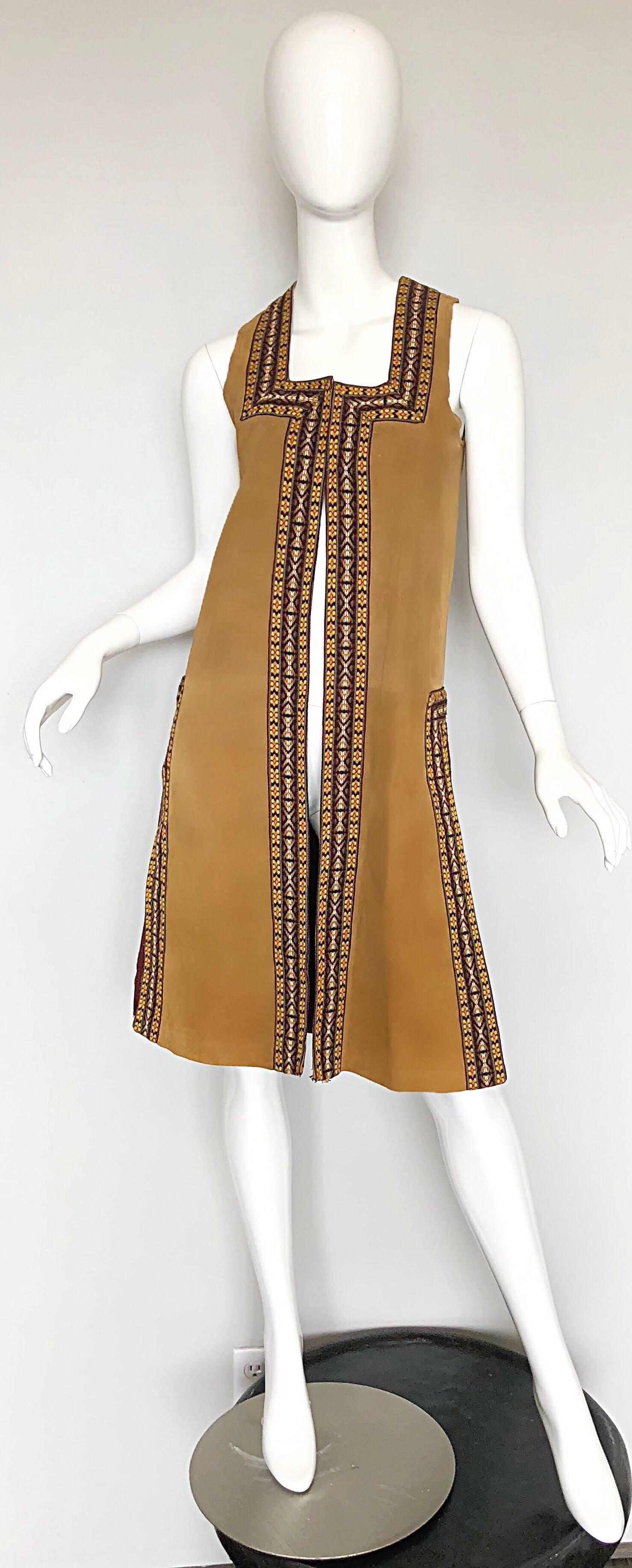 Chic 1970s tan suede embroidered knee length boho vest! Features hand embroidered edges in orange, yellow, green, brown and ivory. Two hook-and-eye closures at bust. Vents at each side of the hem. Fully lined. Fantastic tailored fit. The perfect