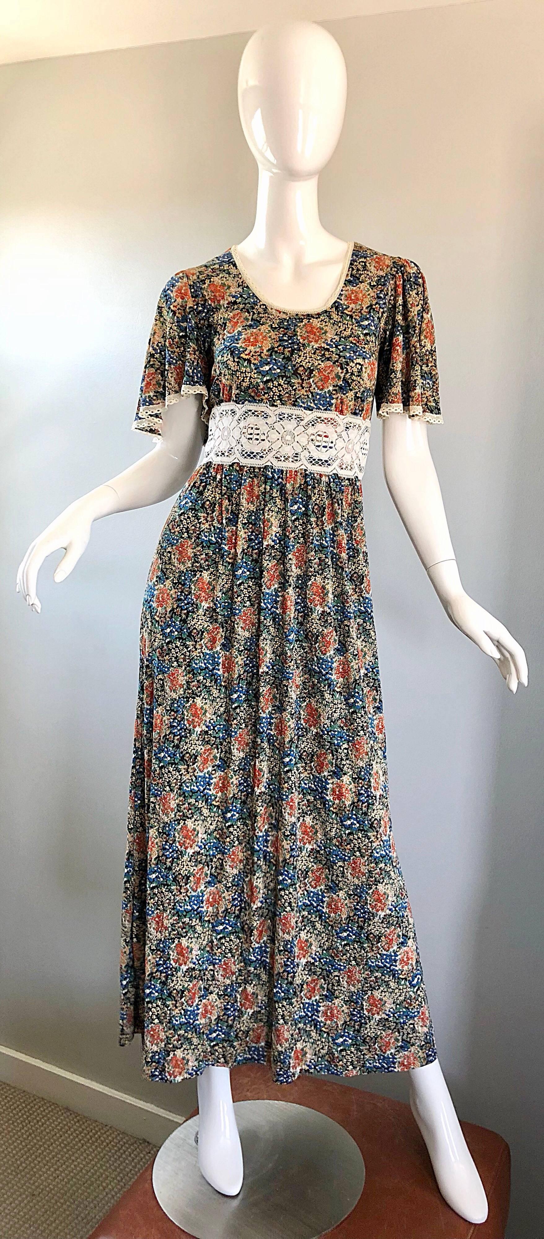 Amazing 1970s boho flower print jersey and lace maxi dress! Features warm tones of blue, green, orange, beige and ivory throughout. Various prints of different flowers. Chic flutter sleeves look great on! Self tie belt ties in the back, and allows