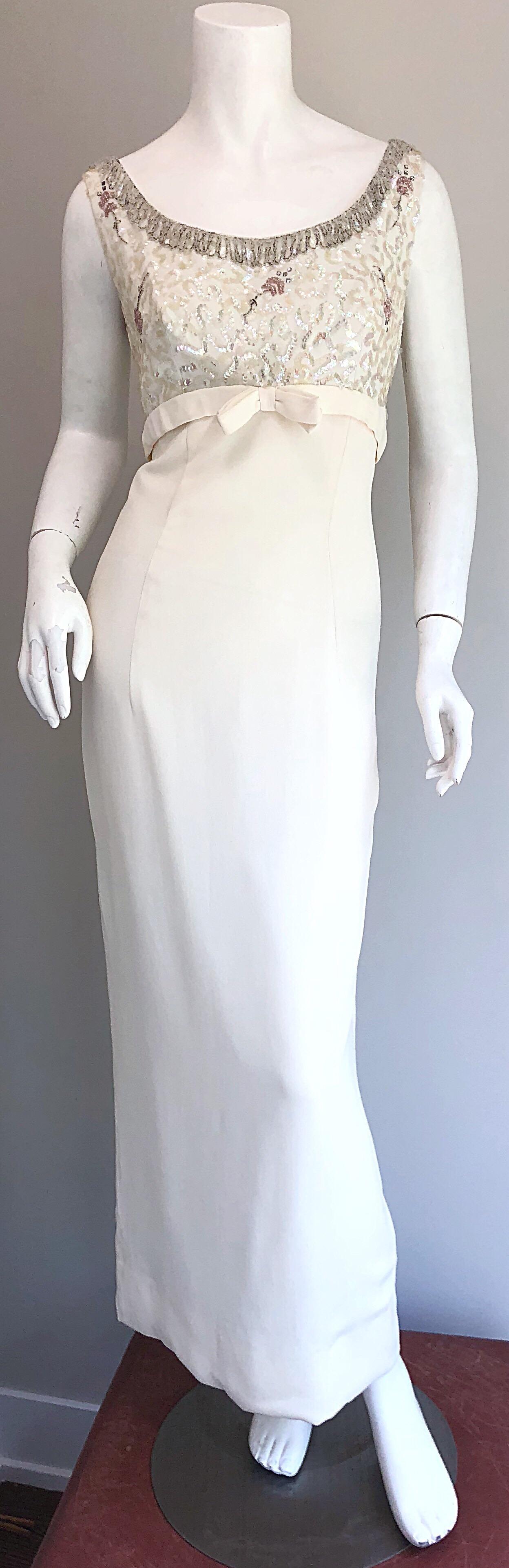 Gorgeous early 1960s white crepe sequined and beaded full length sleeveless evening dress! Features a fitted bodice with hundreds of hand-sewn iridescent sequins and beads. Tassel fringe beaded detail along the neck. Chic bow detail at empire waist.