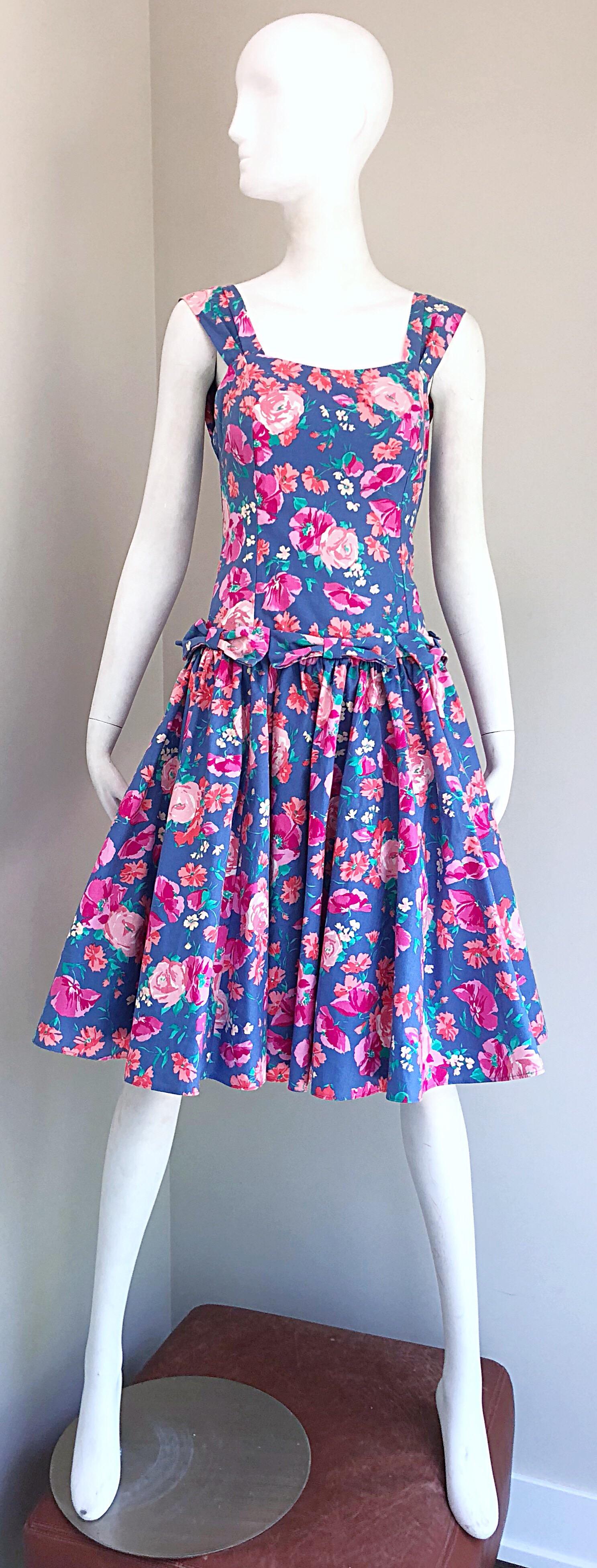 Beautiful 1980s does 1950s LAURA ASHLEY fit and flare cotton dress! Features a periwinkle blue background with pink and hot pink flowers throughout. Interior boned bodice keeps everything in place. Chic bows around the entire waist. Attached purple