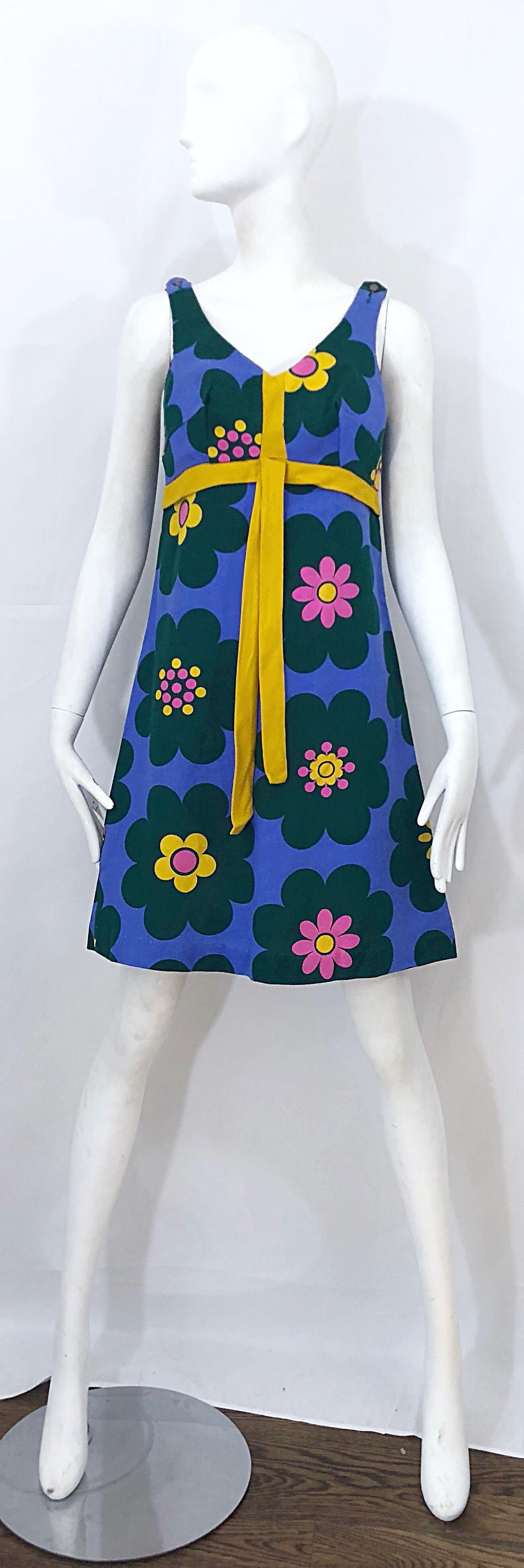 Chic 60s linen flower print sleeveless A-Line dress! Features a purple background, with pink, yellow and green flowers printed throughout. Tailored bodice with a flared skirt. Attached marigold tie detail at waist. Full metal zipper up the back with
