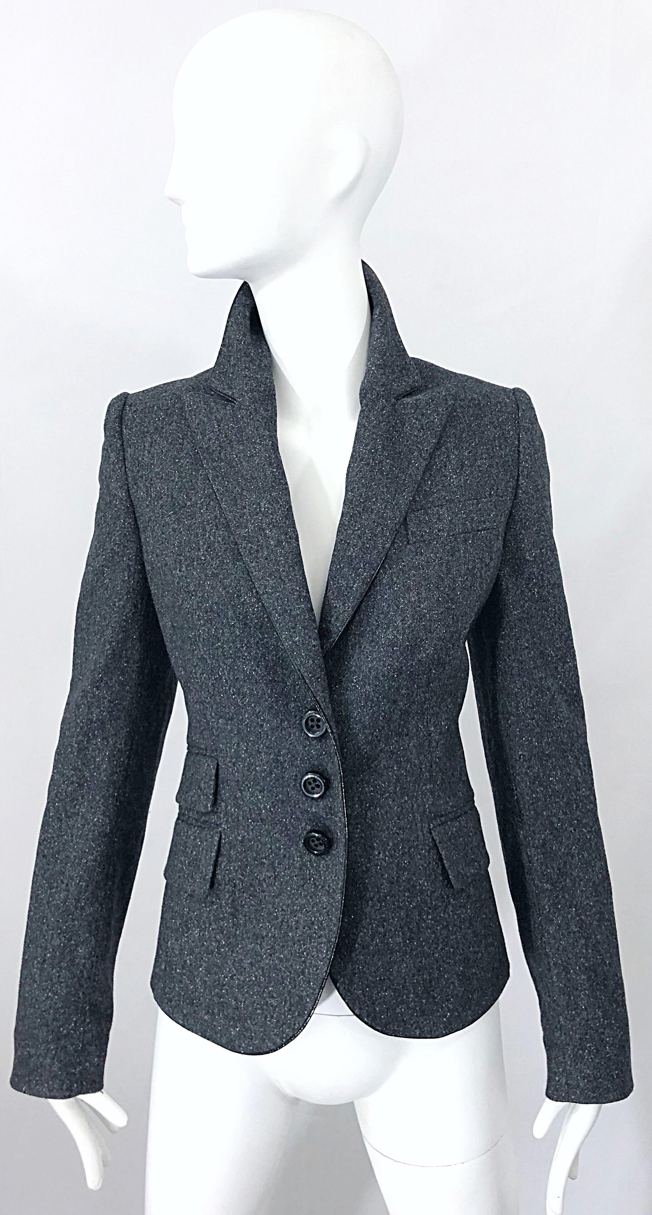 Stylish new JOHN RICHMOND X grey fitted slim fit blazer jacket! Smart tailoring, with three buttons up the front, two pockets at the right side of the waist, and one on the left. Black PVC piping along the trim of the collar, lapels, and edges.