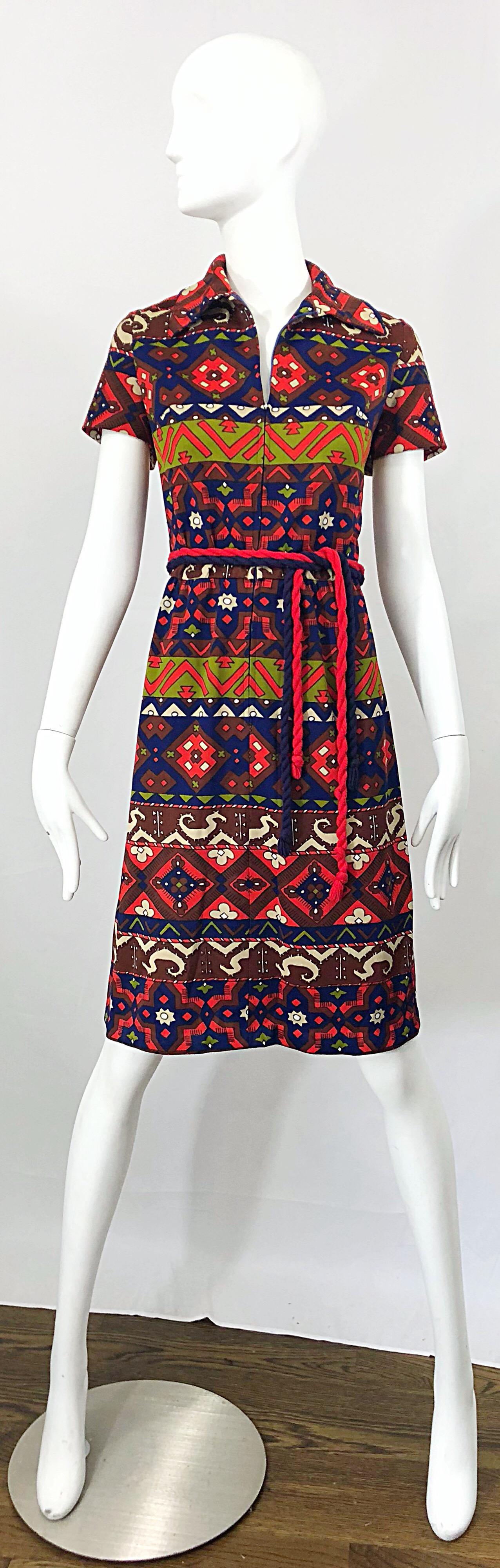 Amazing vintage Aztec inspired 1970s knit belted shirt dress! Features warm tones of red, chartreuse green, navy blue and maroon throughout. Zips up the front to control cleavage. Two tassel belts in red and navy. Great with heels, sandals, wedges,