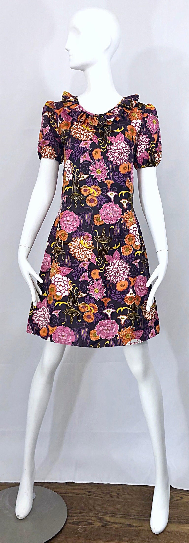 Chic late 1960s lotus orchid novelty flower print short puff sleeve vintage A-Line dress! Features a dark purple background with bubblegum pink, orange, yellow, and lavender purple lotus, orchids and flowers printed throughout. Ruffled collar and