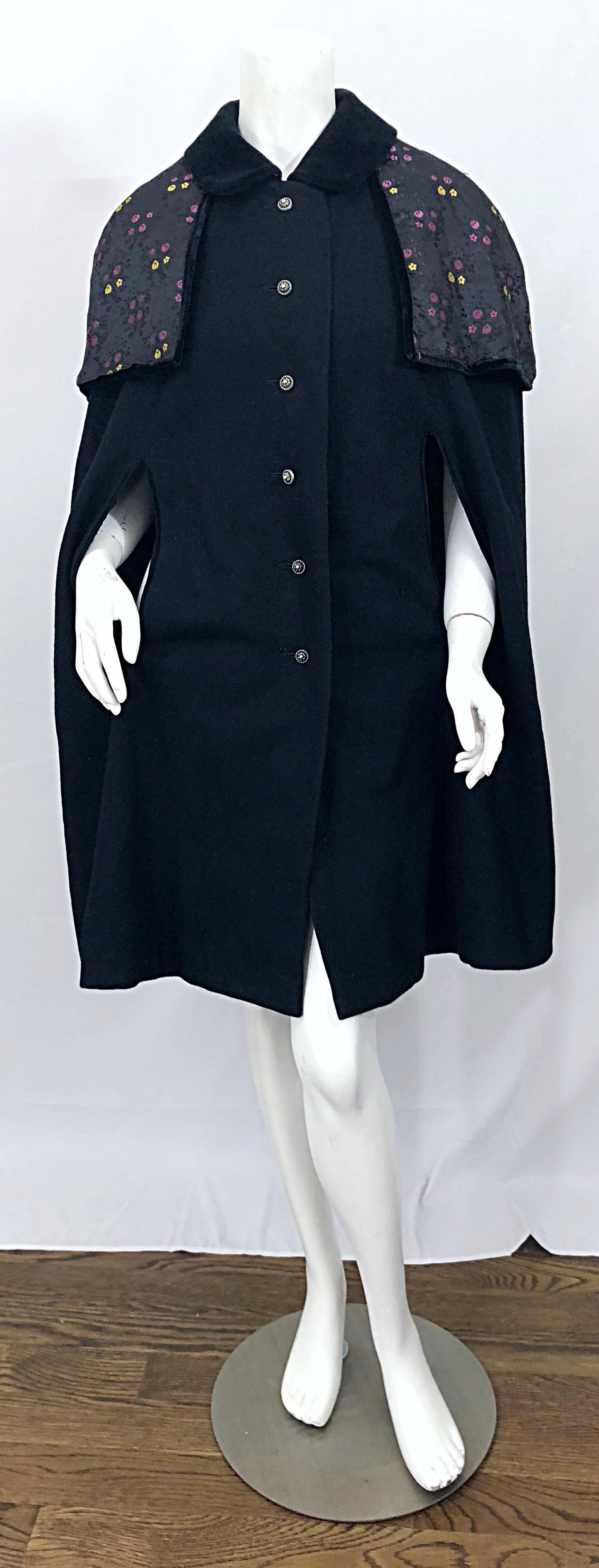 Schickes schwarzes Wollcape aus den 1960er Jahren mit abnehmbarem Kragen und Kapuze! Weiche Schurwolle mit Samtkragen. Abnehmbarer Schal / Kragen kann mit versteckten Knöpfen abgenommen werden. Nickelgeprägte Knöpfe auf der Vorderseite. Sehr gut