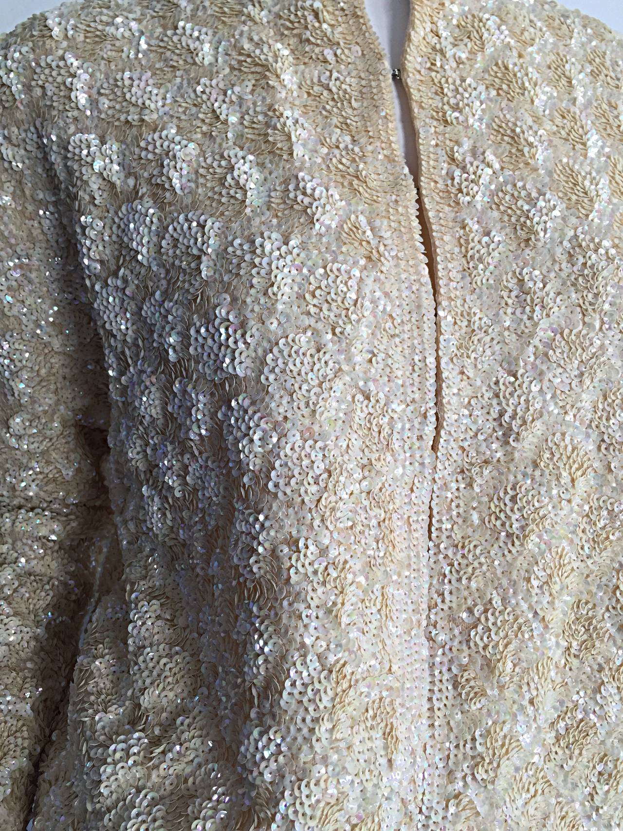 Wunderschöne elfenbeinfarbene Wolljacke aus den 1960er Jahren! Allseitig schillernde Pailletten. Haken- und Ösenverschlüsse vorne. Kann mit Jeans oder über einem Cocktailkleid getragen werden. Sieht auch mit Gürtel toll aus. Vollständig gefüttert.
