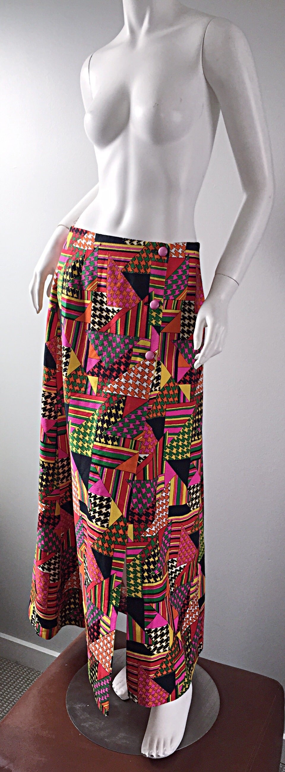 Amazing late 1960s / early 1970s cotton Maxi skirt! Features multi color geometric shapes throughout, with houndstooth accents. Pink buttons up the side. 100% Cotton. In great condition. Approximately Size Medium

Measurements:
30 inch waist
46