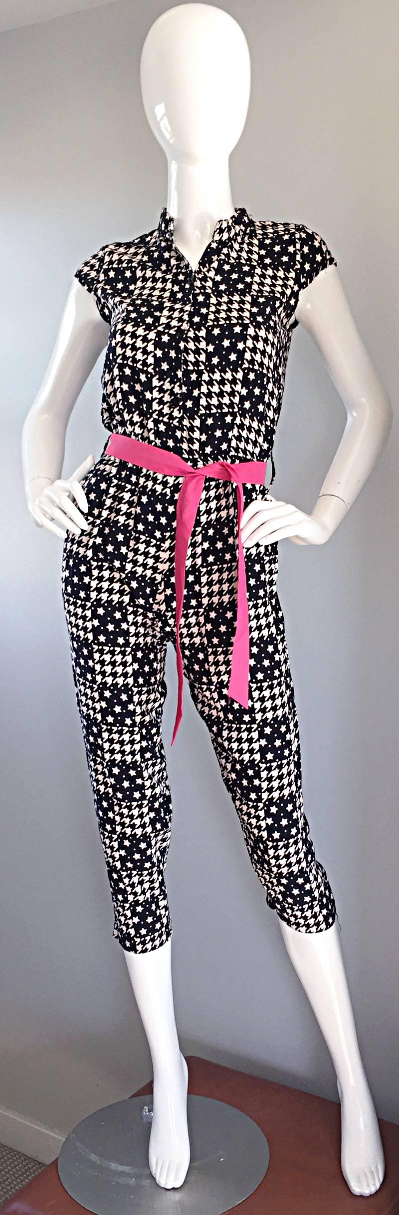Toller 80er-Jahre-Jumpsuit im Vintage-Look! Wunderschönes Hahnentrittmuster, gemischt mit Sternen, in Marineblau und Weiß. Abnehmbarer rosa Schärpengürtel. Das Mieder ist mit Knöpfen verschlossen. Schlank geschnittene Beine. Taschen auf beiden