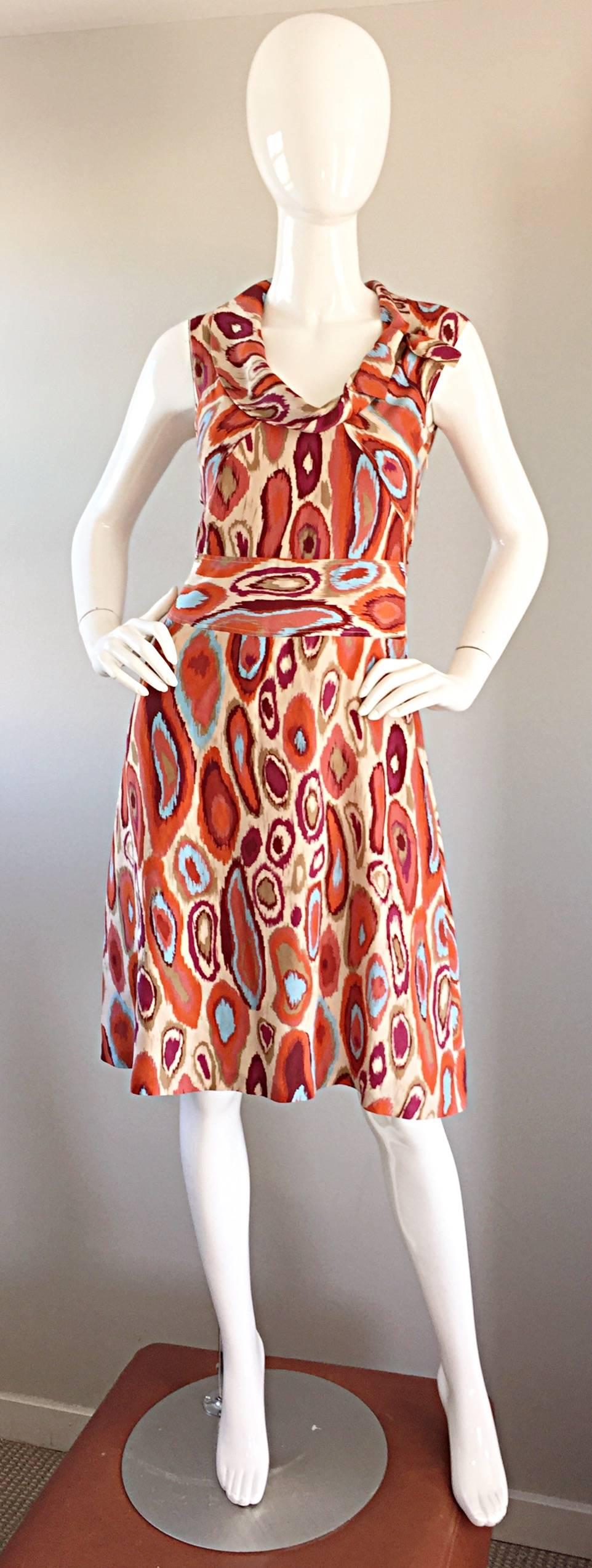 Neuf avec étiquettes CACHAREL Robe en soie imprimée Ikat style années 1960 ! Il présente des tons chauds d'orange brûlé, de brun, de bordeaux et de bleu ciel. Col bénitier chic avec nœud discret. Une coupe légèrement A-Line, qui est très flatteuse