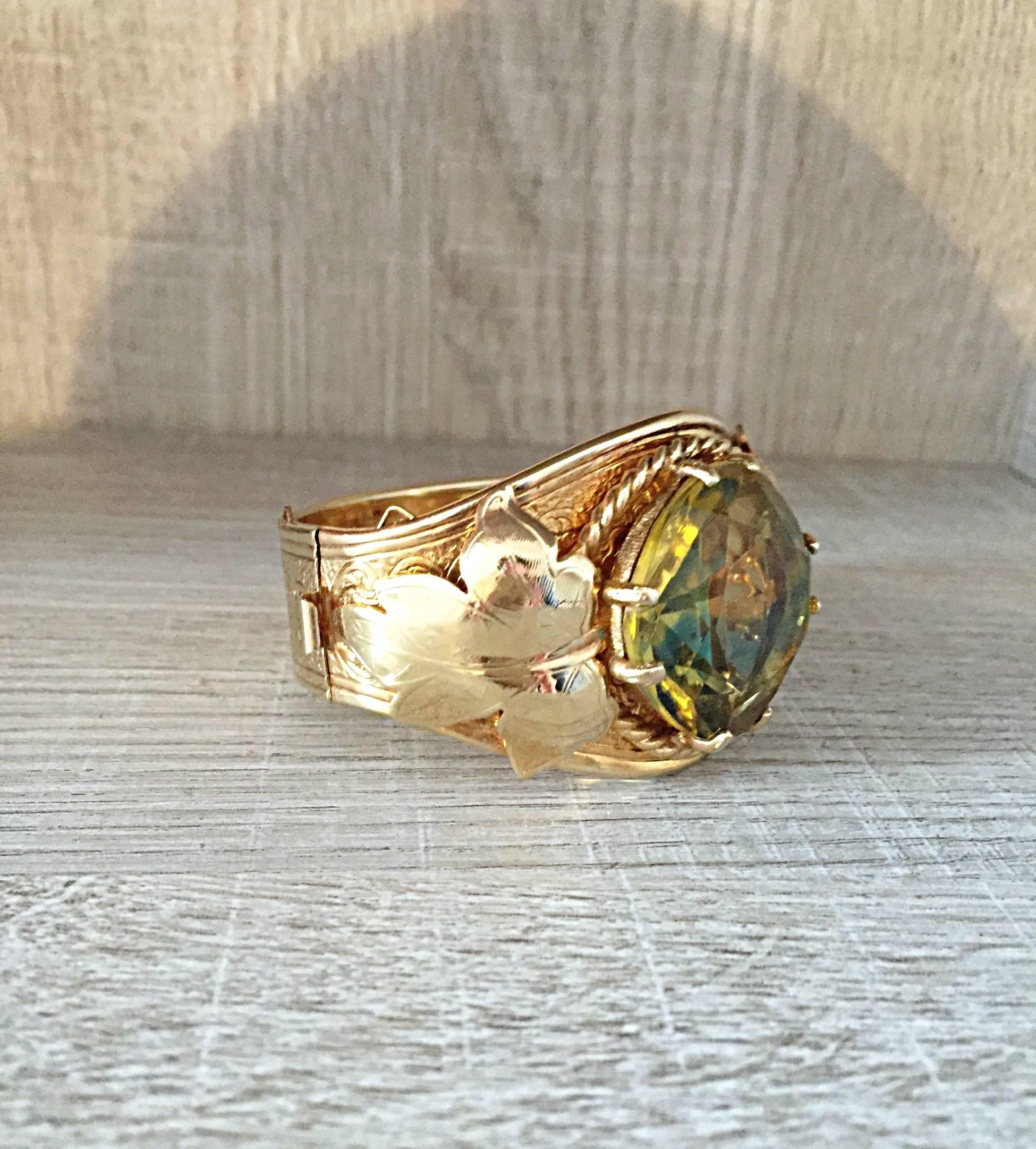 Beautiful 70s Sarah Coventry gold hinged metal bracelet with a large yellow green stone. The bangle is 2 1/4 inches in diameter in the closed position.  It has a 1 1/4 inch diameter stone that is faceted. The stone is held in place by 8 prongs and