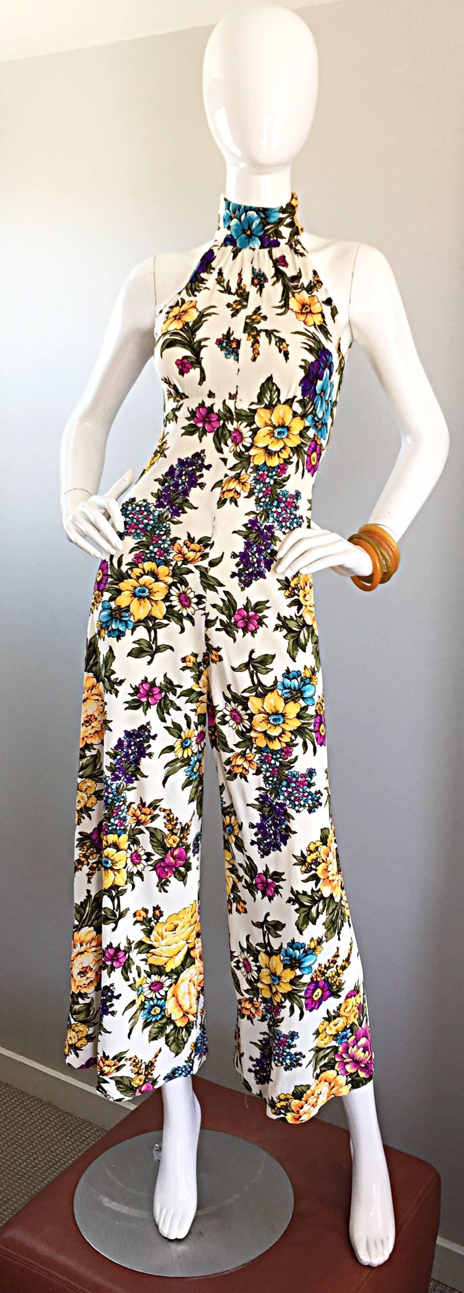 Incredible 1970s cropped wide leg bell bottom halter jumpsuit! Features a white background, with pink, blue, yellow, purple and green flowers printed throughout. Flattering high neck, with a fitted bodice. Looks amazing on! Hidden zipper up the back