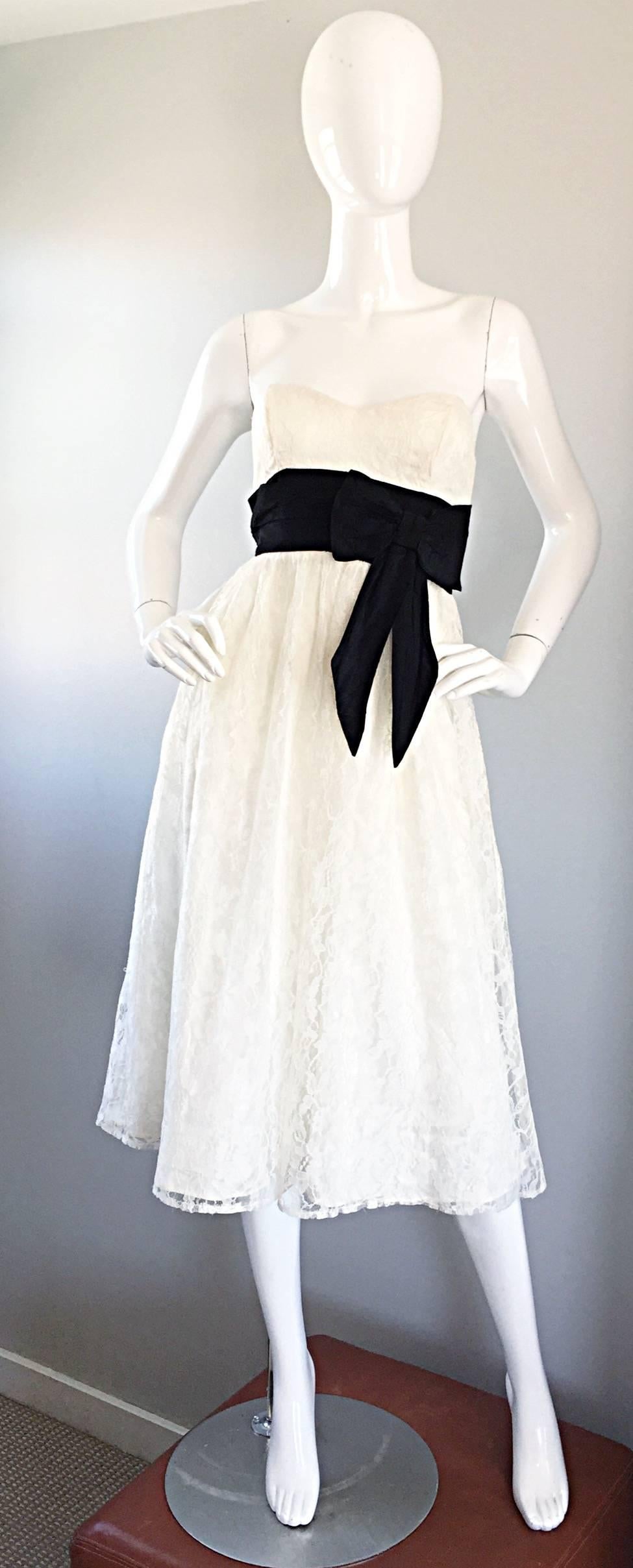 Chic vintage 90s does 50s white and black lace strapless dress! Features white French lace over a silk white underlay. Attached black taffeta origami layered belt. Full hidden zipper up the back. Strapless sweetheart neckline. Interior boning on the