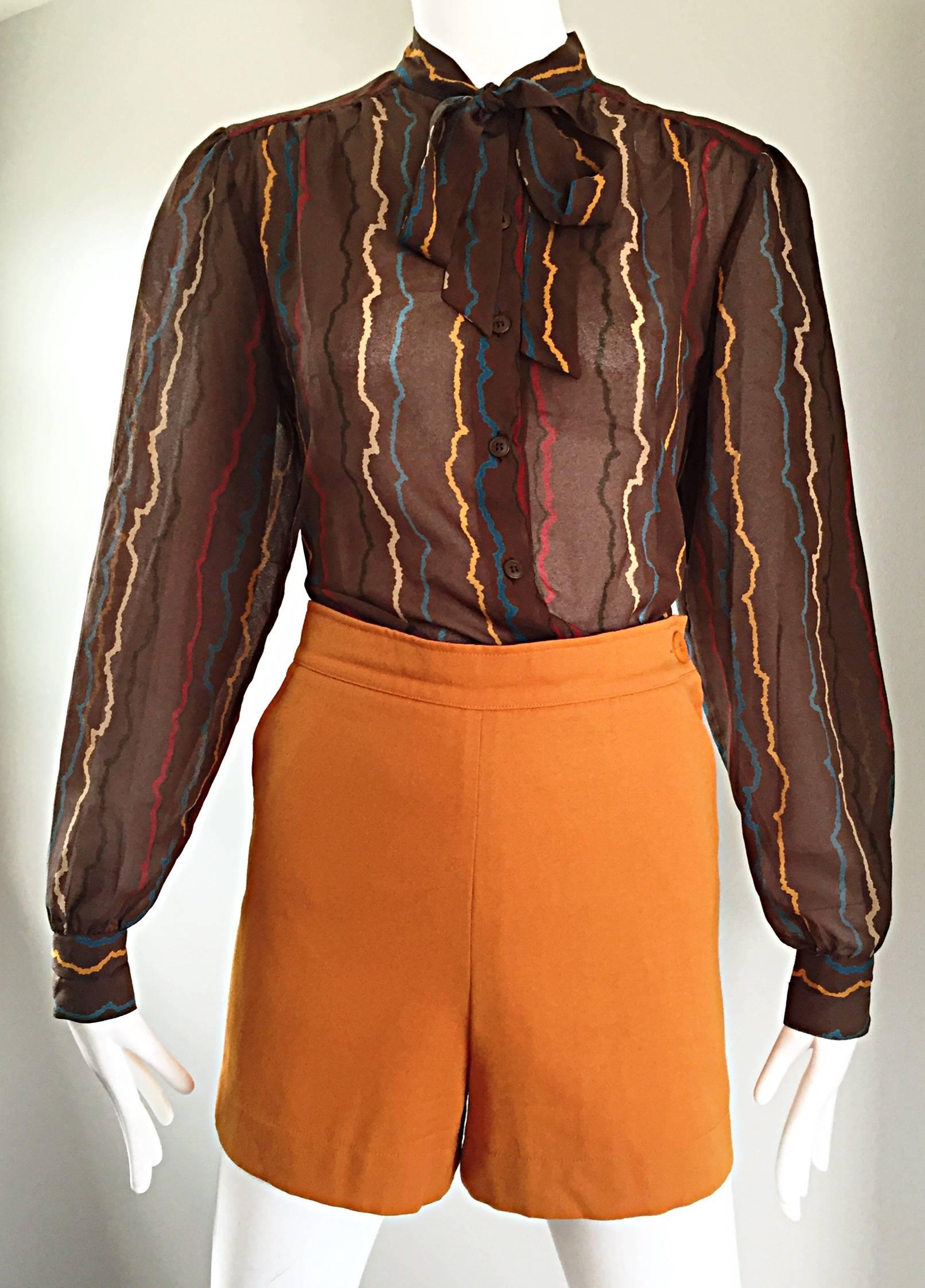 Chic blusa vintage anni '80 MONDI in seta semi trasparente color tortora con fiocco Pussycat! Presenta delle fasce di colore in giallo, rosso, blu, tortora e nero. Il corpetto è abbottonato e il collo è dotato di un fiocco da annodare. Bottoni su