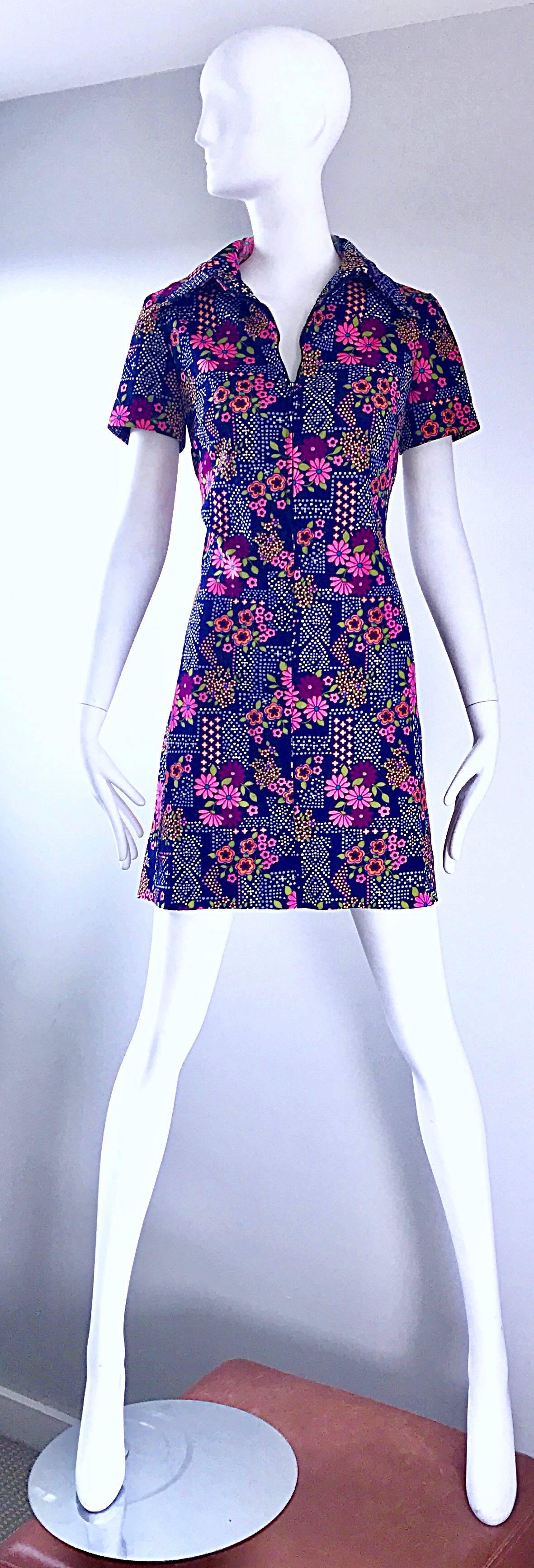 Such a chic 1960s colorful daisy printed mini shirt shift dress! Features a navy blue knit, with colorful daisies and geometric shapes throughout. Vibrant colors of pink, green, purple, yellow and orange throughout. Pointed collar, with a zipper up