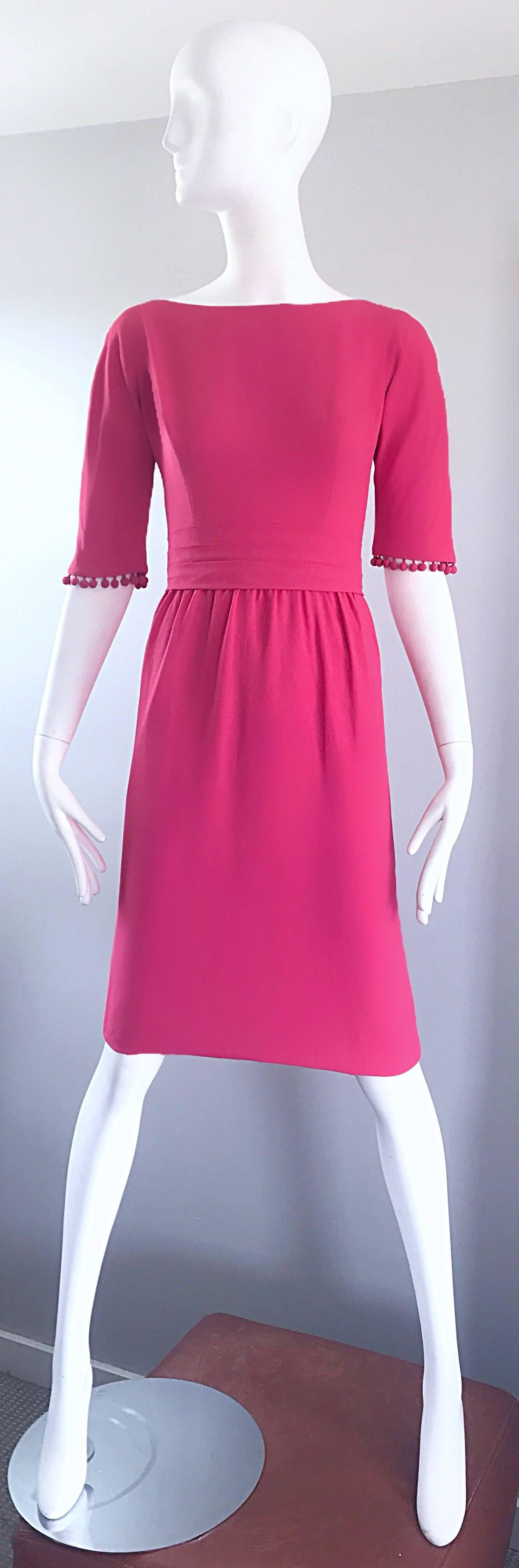 Magnifique robe demi-couture des années 1950 en crêpe rose framboise ! Des boules de pom pom sont attachées aux poignets de chaque manche. Des pompons figurent également sur la traîne dans le dos. Fermeture à glissière entièrement métallique dans le