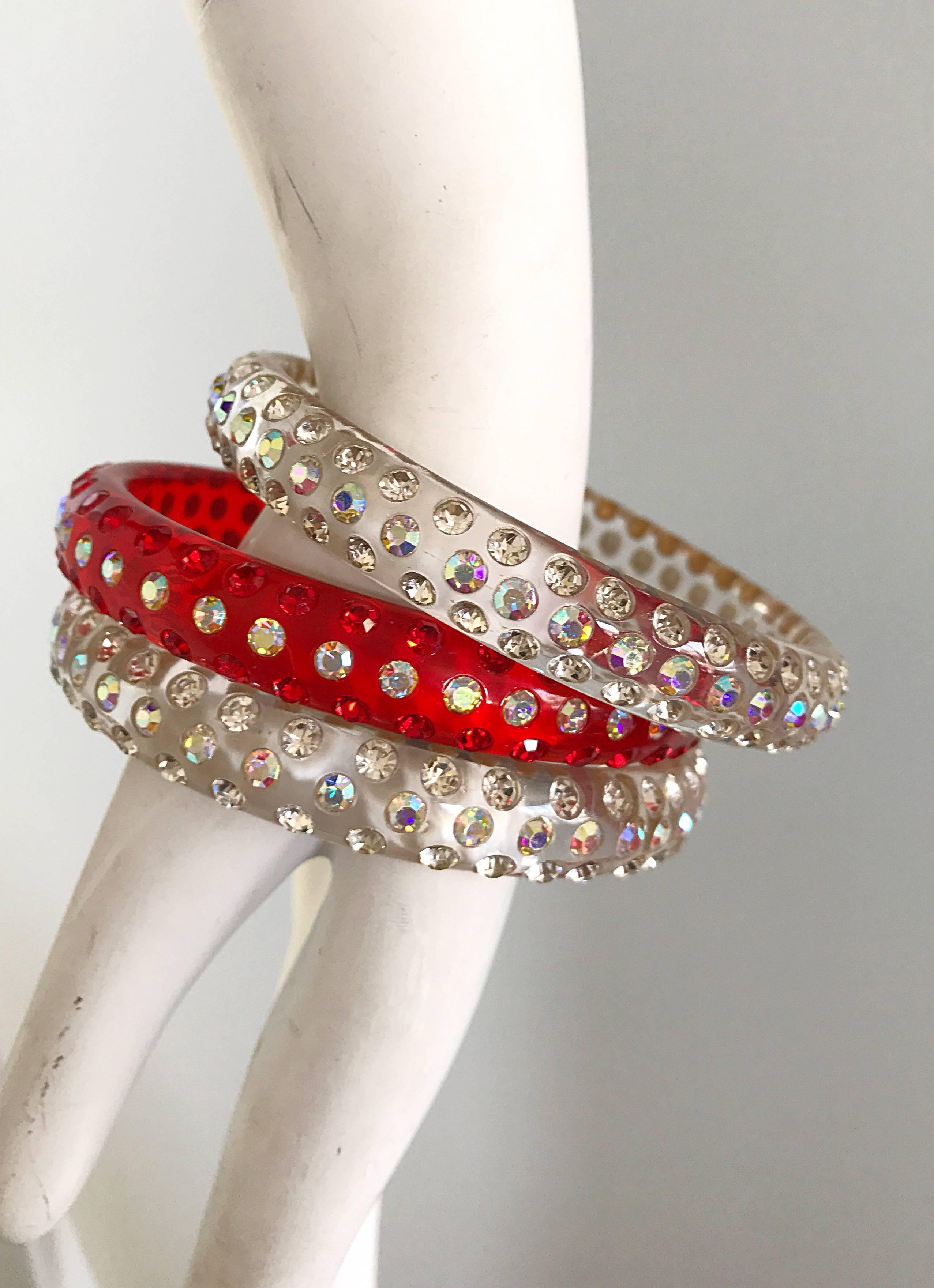 Lovely set of three red and clear lucite rhinestone encrusted bangle bracelets! Set consists of two clear bangles and one red one. Clear ones feature three rows of rhinestones, and red one features one row of rhinestones in the center, and two rows