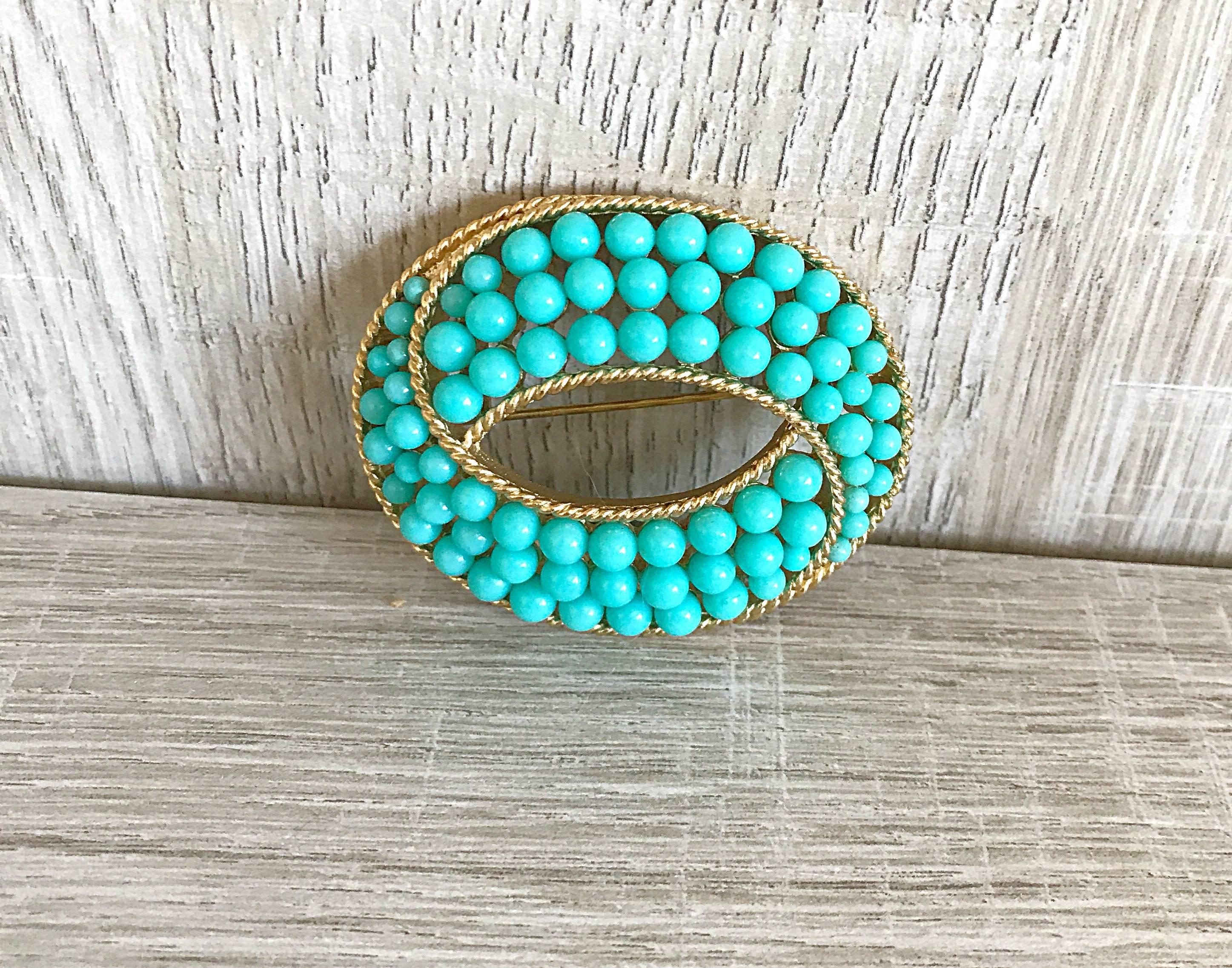 Chic and beautiful 1960s TRIFARI turquoise and gold oval ball brooch! Features turquoise beads with a gold etched frame. Trifari stamped on the back.         The perfect accessory to add a little something extra to any outfit! Great on a jacket,