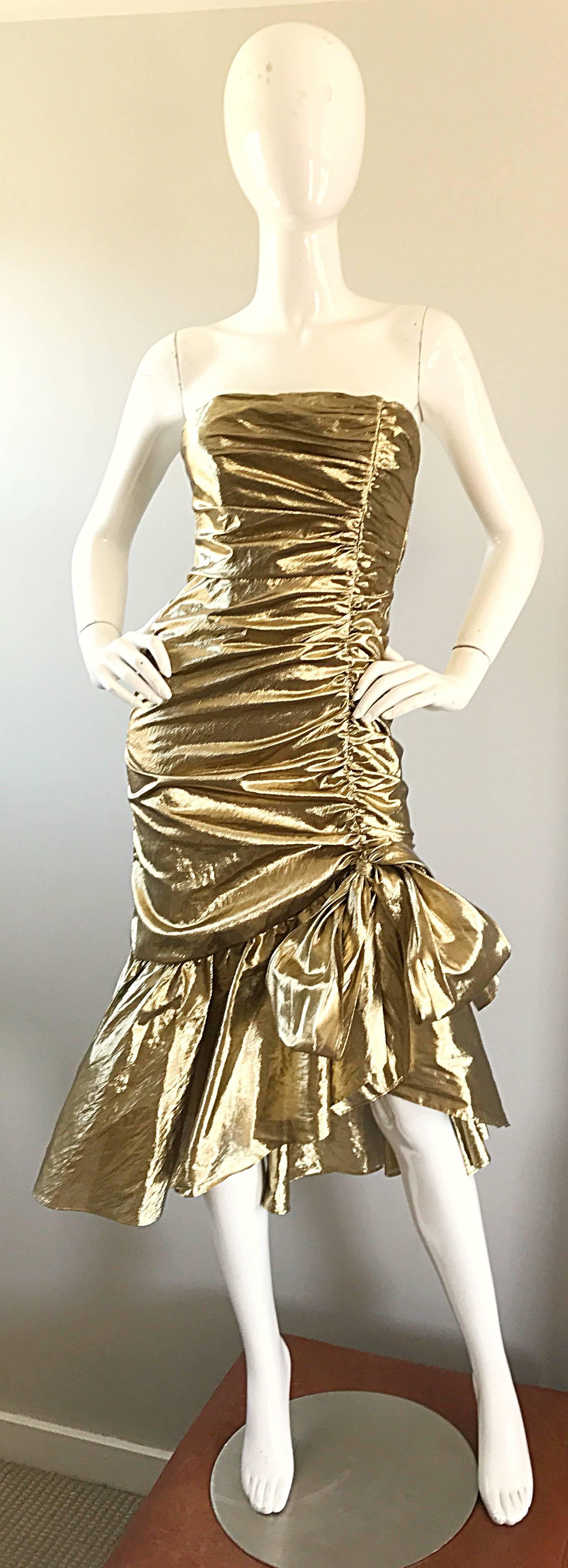 Amazing 1980s gold lame strapless Avant Garde cocktail dress! Features flattering ruched body, with an asymmetrical flared mermaid hem. Two panels tie to form a bow at the left hem. Hidden zipper up the back. Great belted or alone with heels or