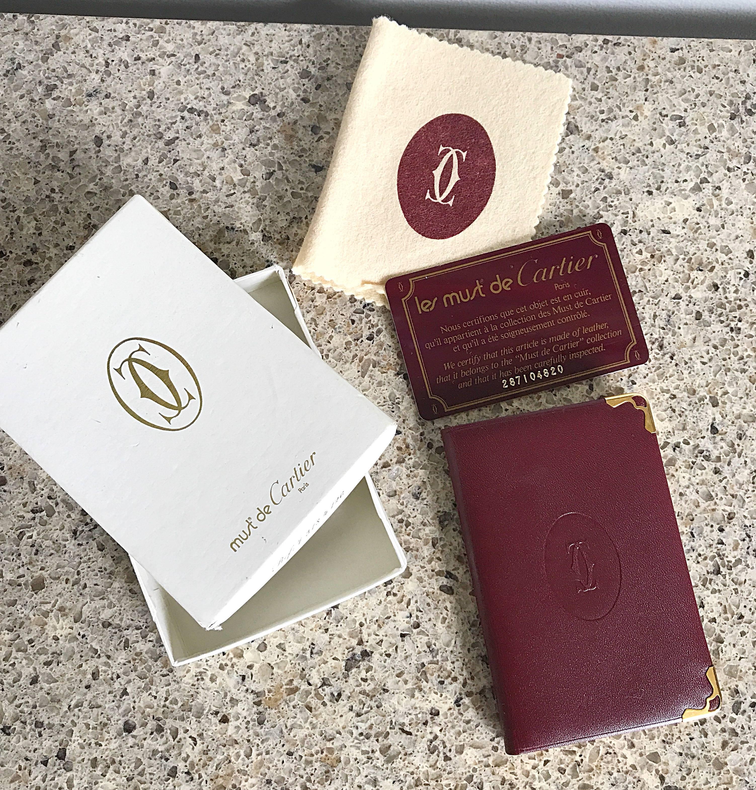 Brand new in box LE MUST de CARTIER burgundy leather small address book! Features four front and back blank pages fro each letter of the alphabet (for a total of eight pages for each letter). Front of the address book is embossed with the Cartier CC