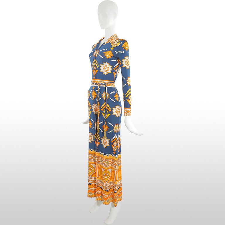 This gorgeous early 70’s full length dress from Leonard Paris is made from printed jersey and depicts a geometric aztec design in tones of bright orange, mustard yellow and navy. It has full length sleeves with covered buttoned cuffs. This dress has