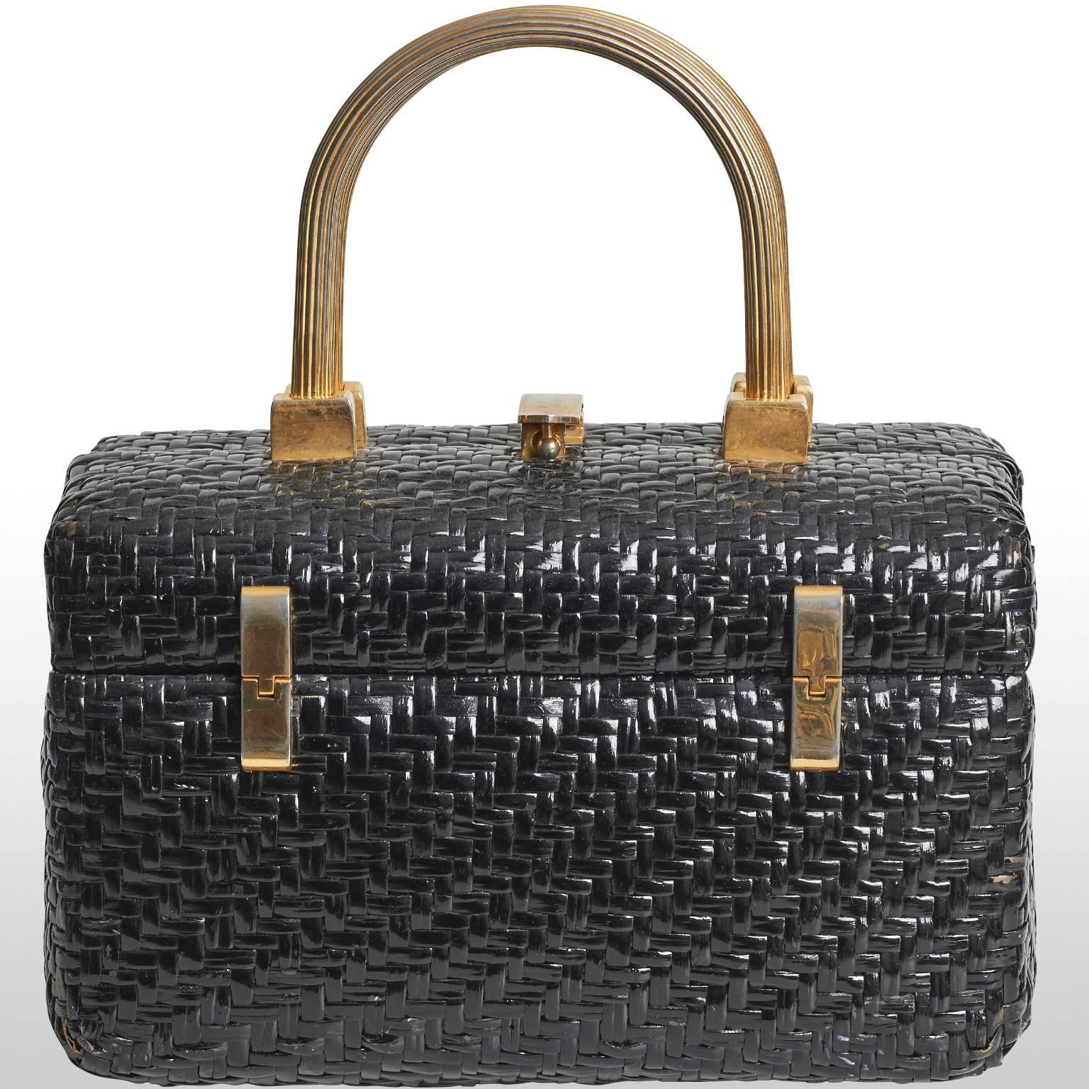 Quirky 1960's box bag with structured gold metal handle.The bag features an interesting woven texture composed of a black wicker material and opens like an old fashioned jewellry box adding a hint of nostalgia. The boxy shape exudes classic 1960s