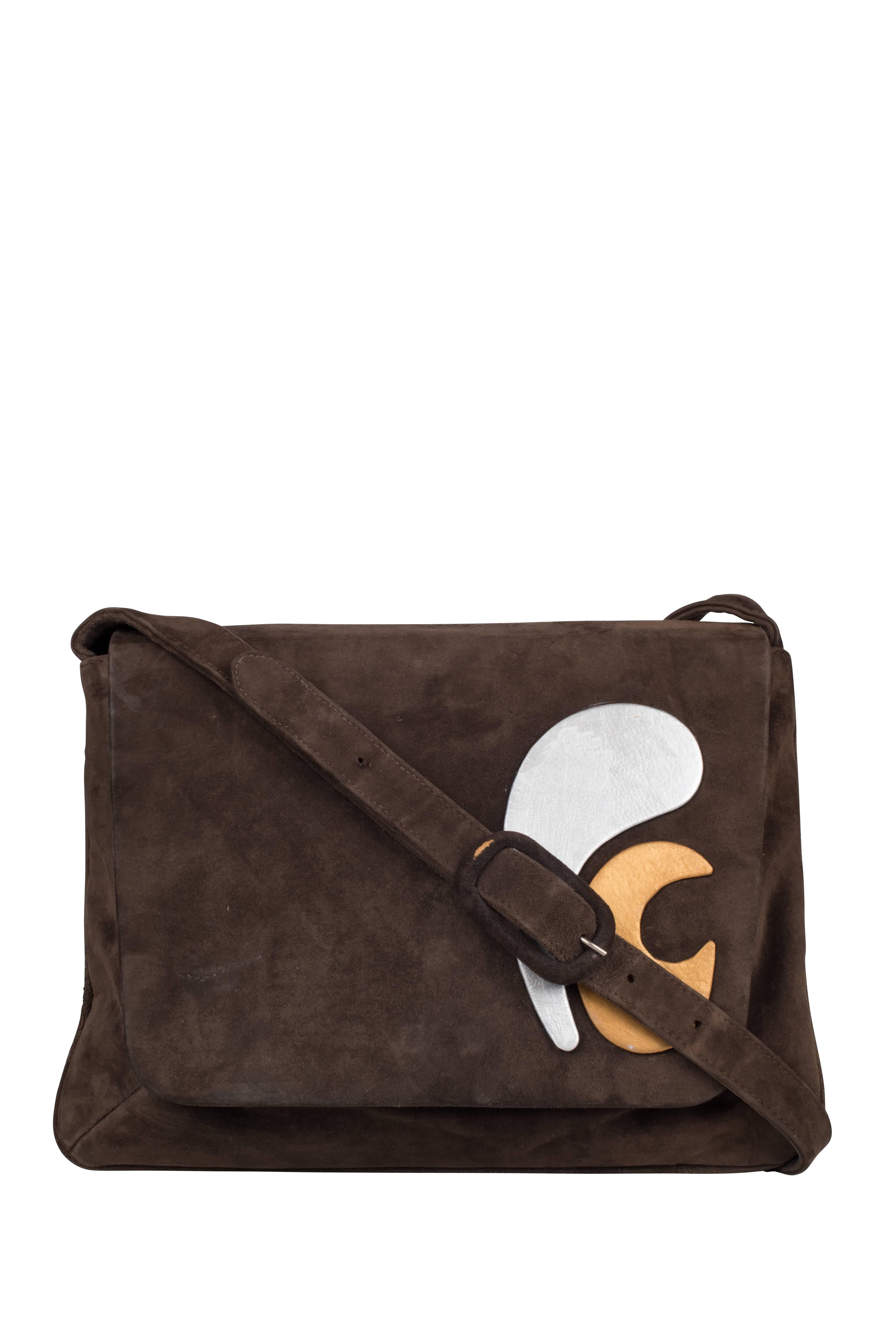 A 1960's brown suede bag by Pierre Cardin. Made from soft brown suede, the bag has an adjustable strap with three holes. The flap is embellished with the designer's initials in space-age leather cut-outs in silver and gold. The inside is made of