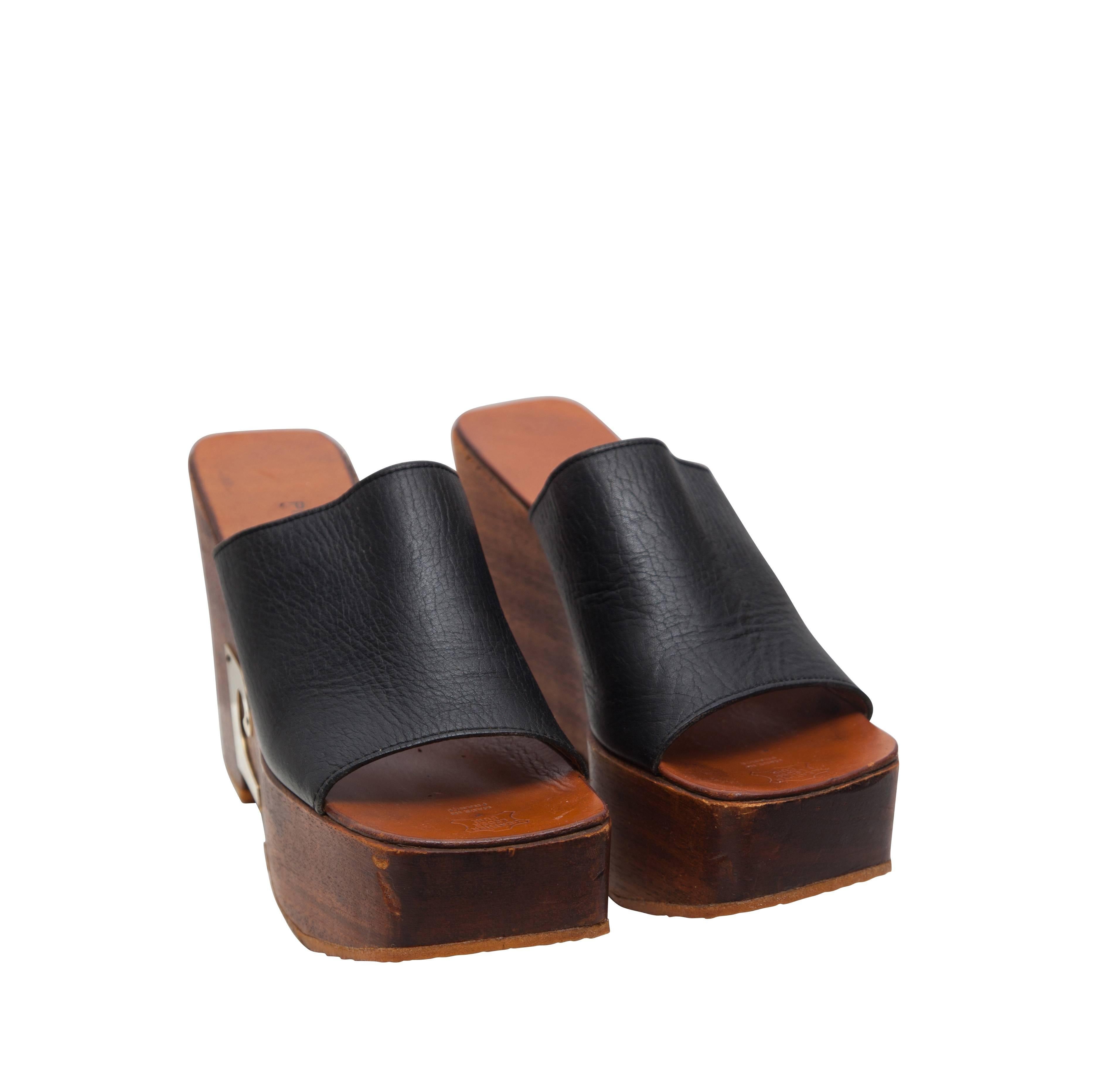 1970's Pierre Cardin wooden heeled wedge shoes, featuring the unmistakable 'PC' logo in golden metal, and wide dark brown leather straps across. The leather on the straps is extremely soft and the wood on the soles shows no sign of wear. Excellent