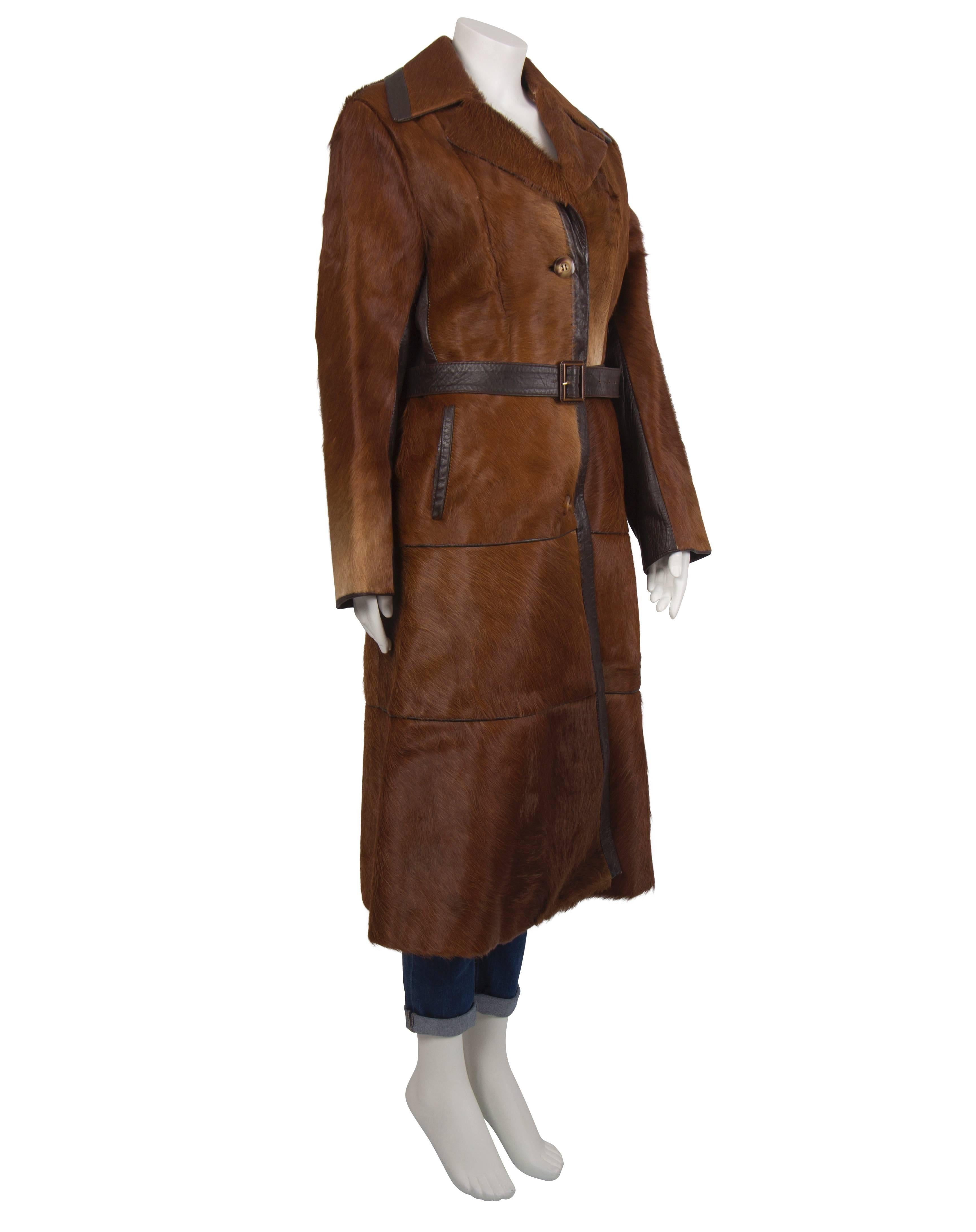 1970's brown pony skin trench coat. The coat buttons on the front with 3 leather covered buttons and the inner side of the sleeves present a dark brown leather insert. Additional features are two pockets on either side along the hip line and a dark