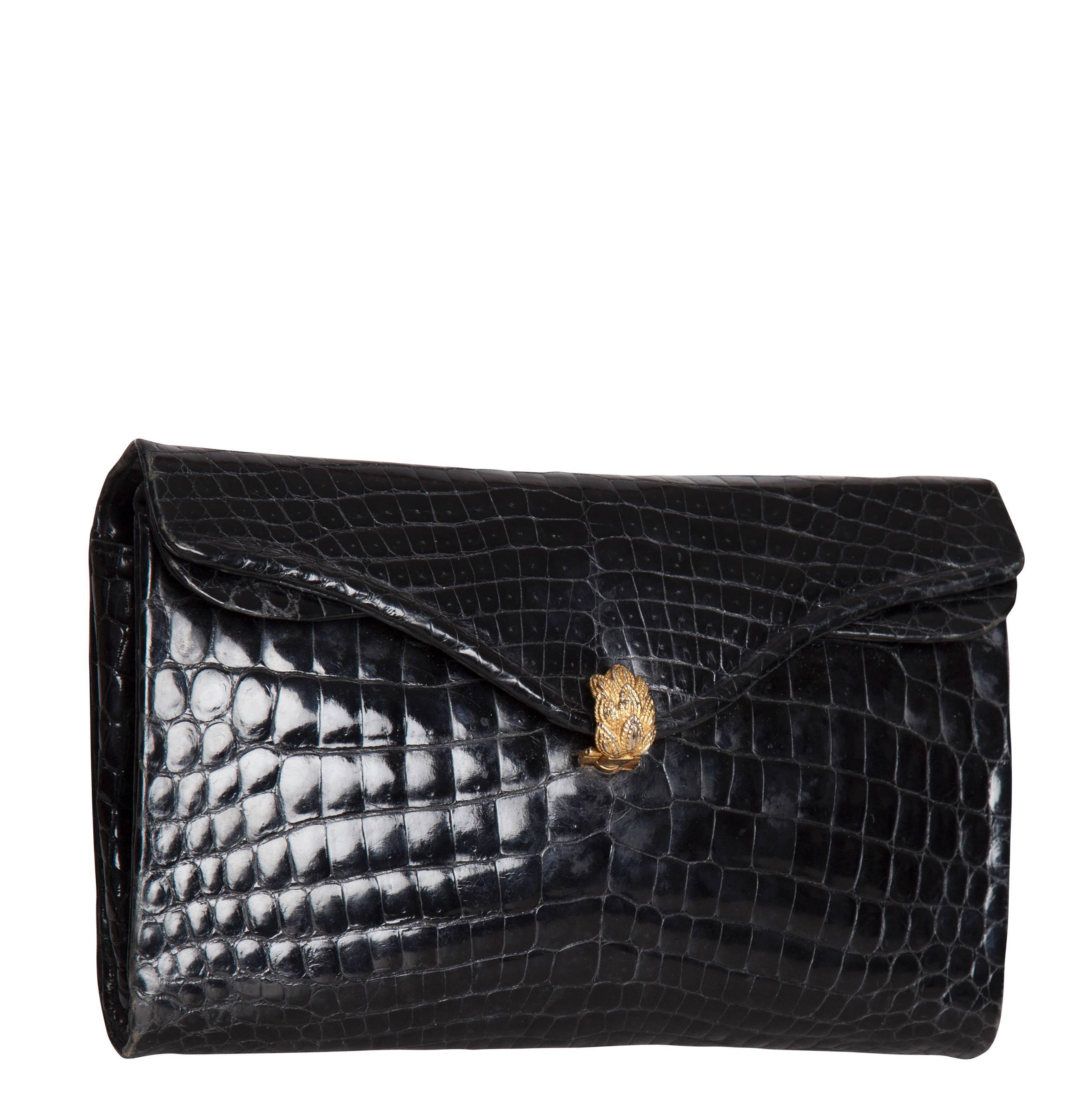 An elegant 1960s black crocodile skin envelope-shaped clutch bag from Parisian luxury leather goods brand Morabito. The bag fastens with a gold-toned curved clasp in the shape of a bunch of leaves. The black leather interior features a zippered