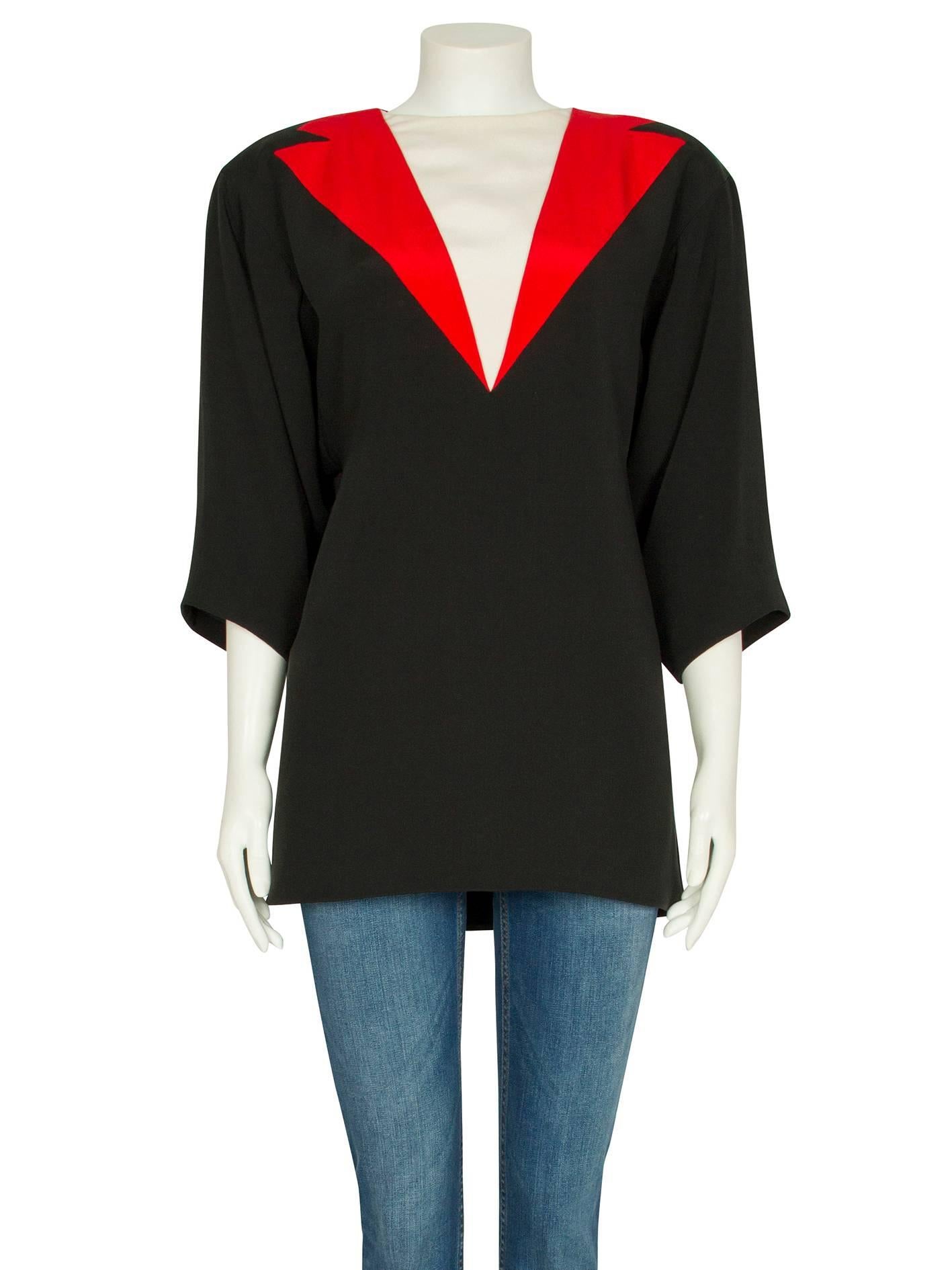 An unusual 1980s Dior Couture black silk tunic top with a red and ivory trompe l’oeil effect neckline. The loose-fitting boxy tunic features padded shoulders and drapey three-quarter-length sleeves, a long hemline and fastens at the back with a row