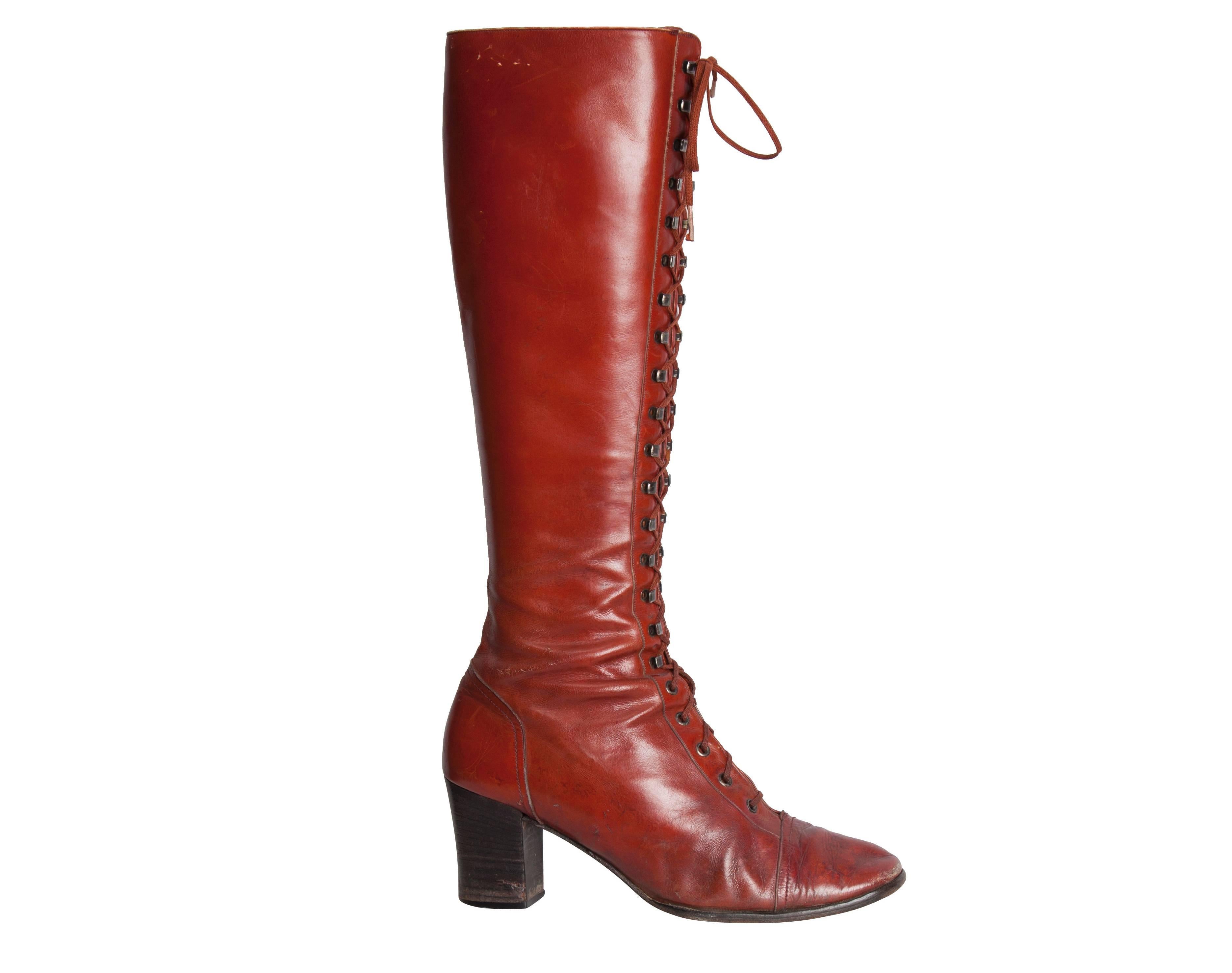 A pair of Yves Saint Laurent Couture brick red leather tall lace-up boots. These mid-calf length boots lace up the entire length of the front using silver metal stud fastenings. They feature a round toe and a chunky black mid-height heel. Excellent