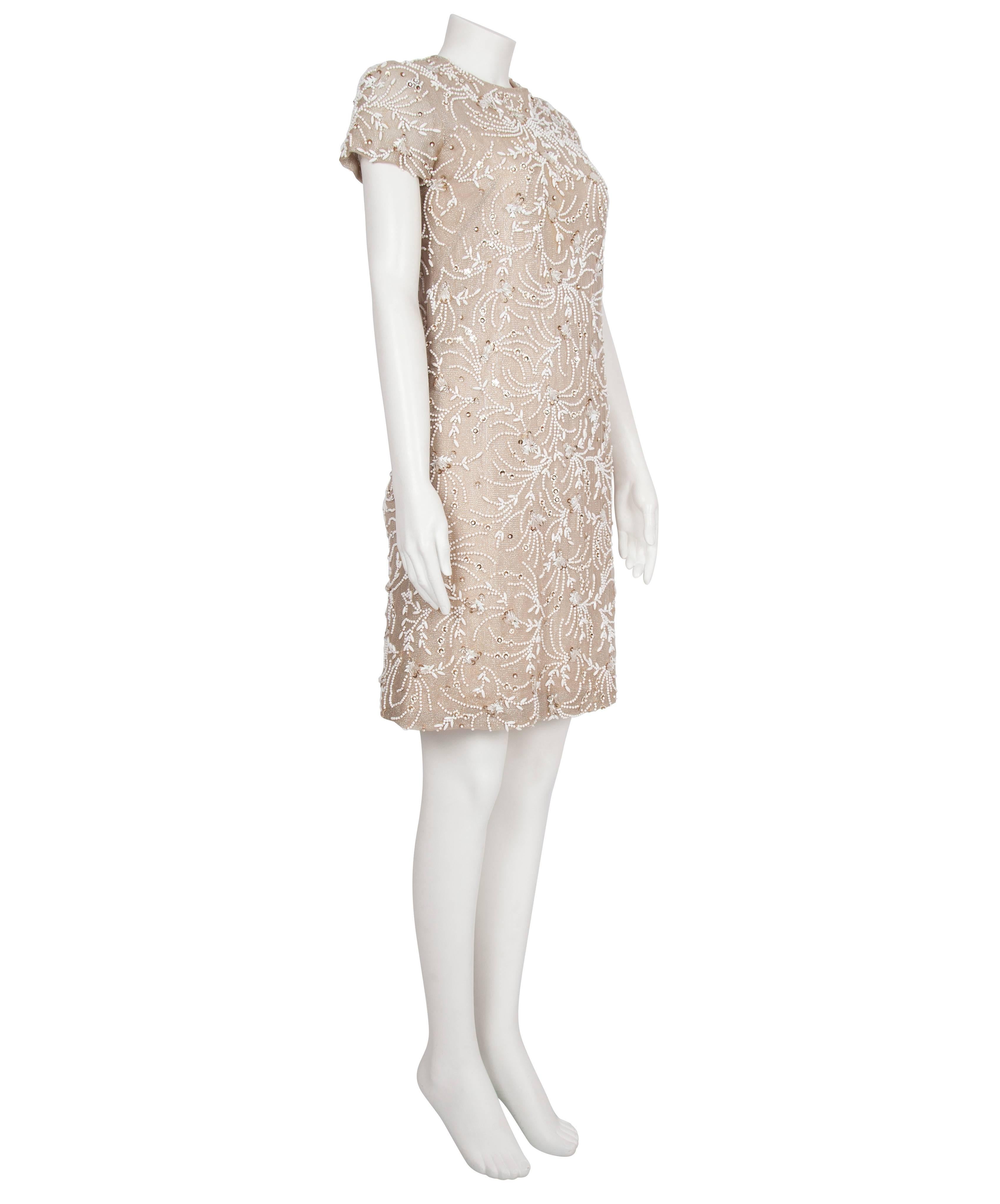 A classic Malcolm Starr 1960's cocktail dress, made from a champagne coloured chiffon covered with a metallic maille embellished with opaque ivory beads. The dress has a crew neck and cap sleeves, and fastens at the back with a zip and a row of