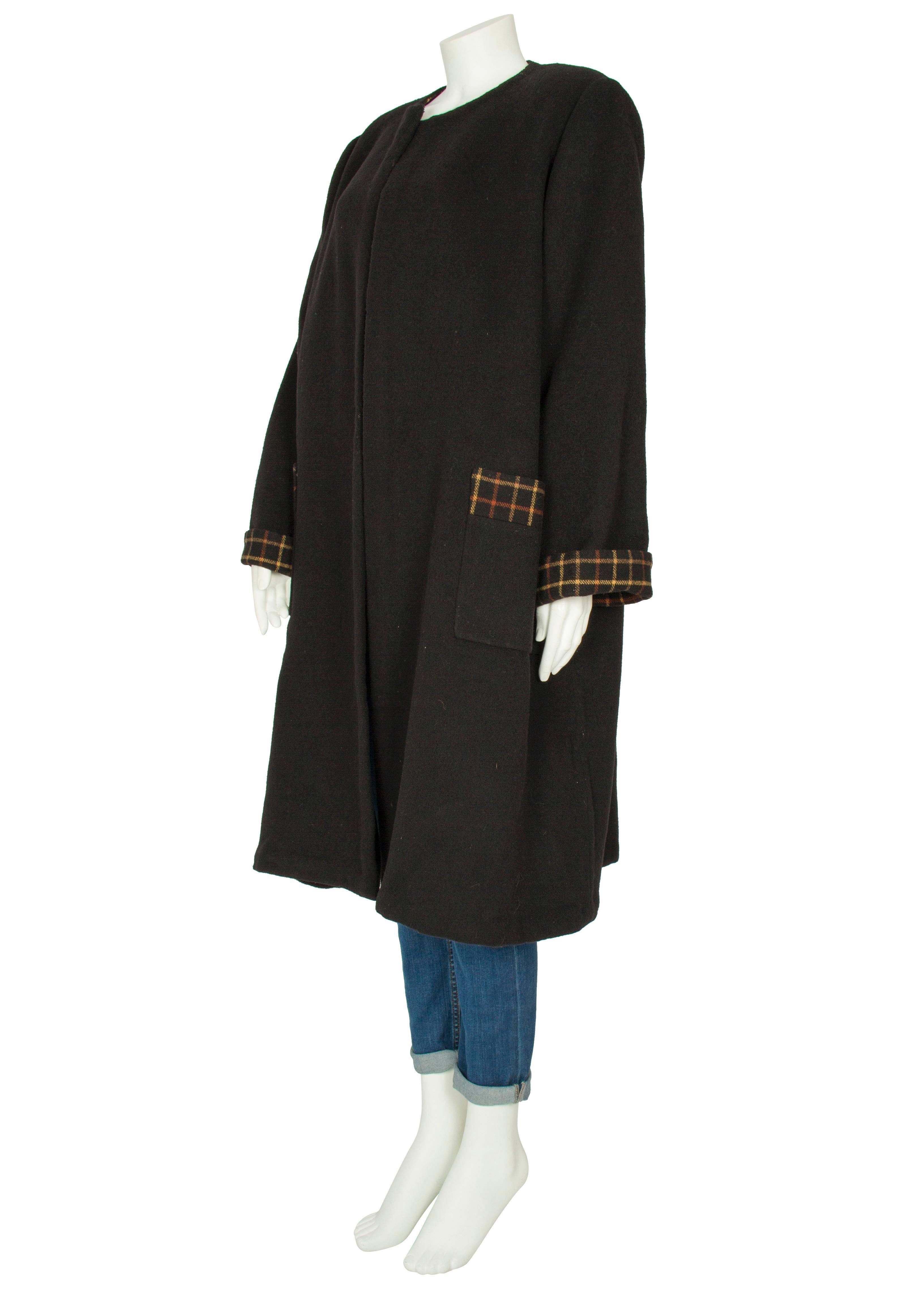 An oversized swing throw-over coat by London society couturier Harald, constructed from a heavy black wool and lined with a brown and caramel checked wool fabric. The mid-length coat is a loose-fitting and collarless design and features long
